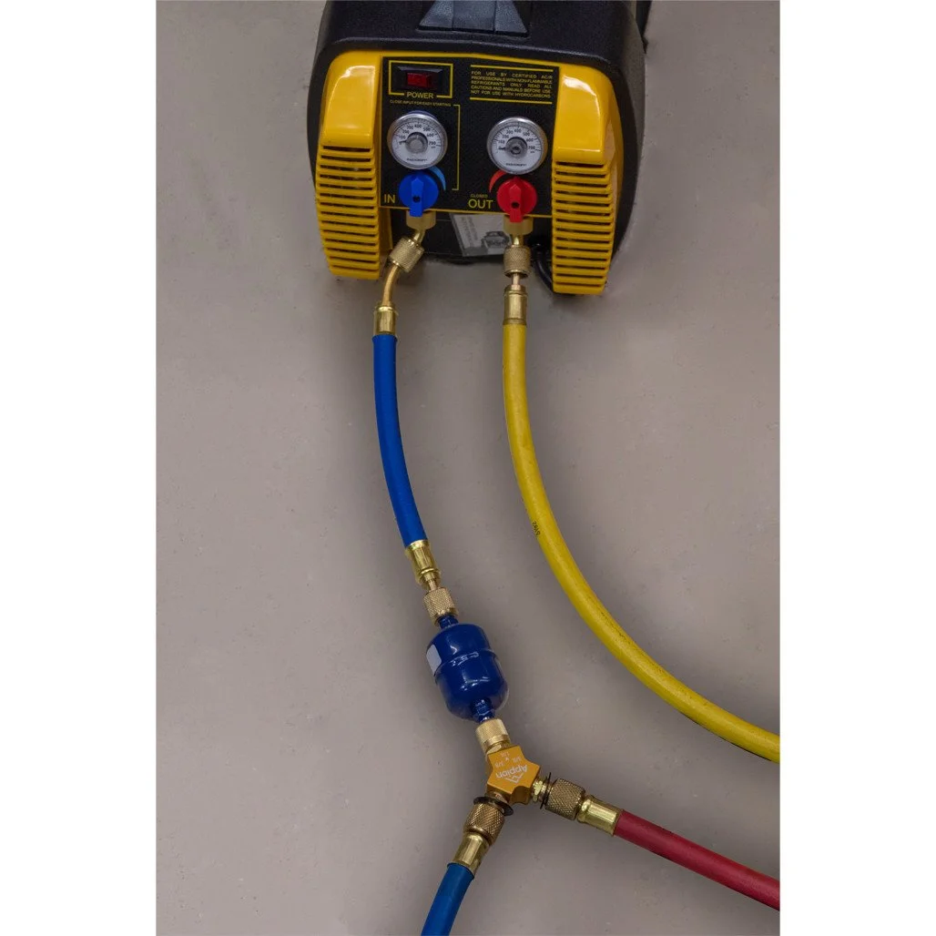 Portable refrigeration or air conditioning unit with yellow hoses connected to blue and red valve fittings on a gray surface.
