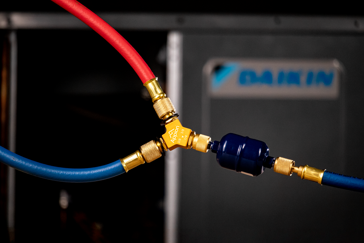 A close-up of red and blue hoses connected through a brass fitting, with a black inline filter, on a piece of machinery.
