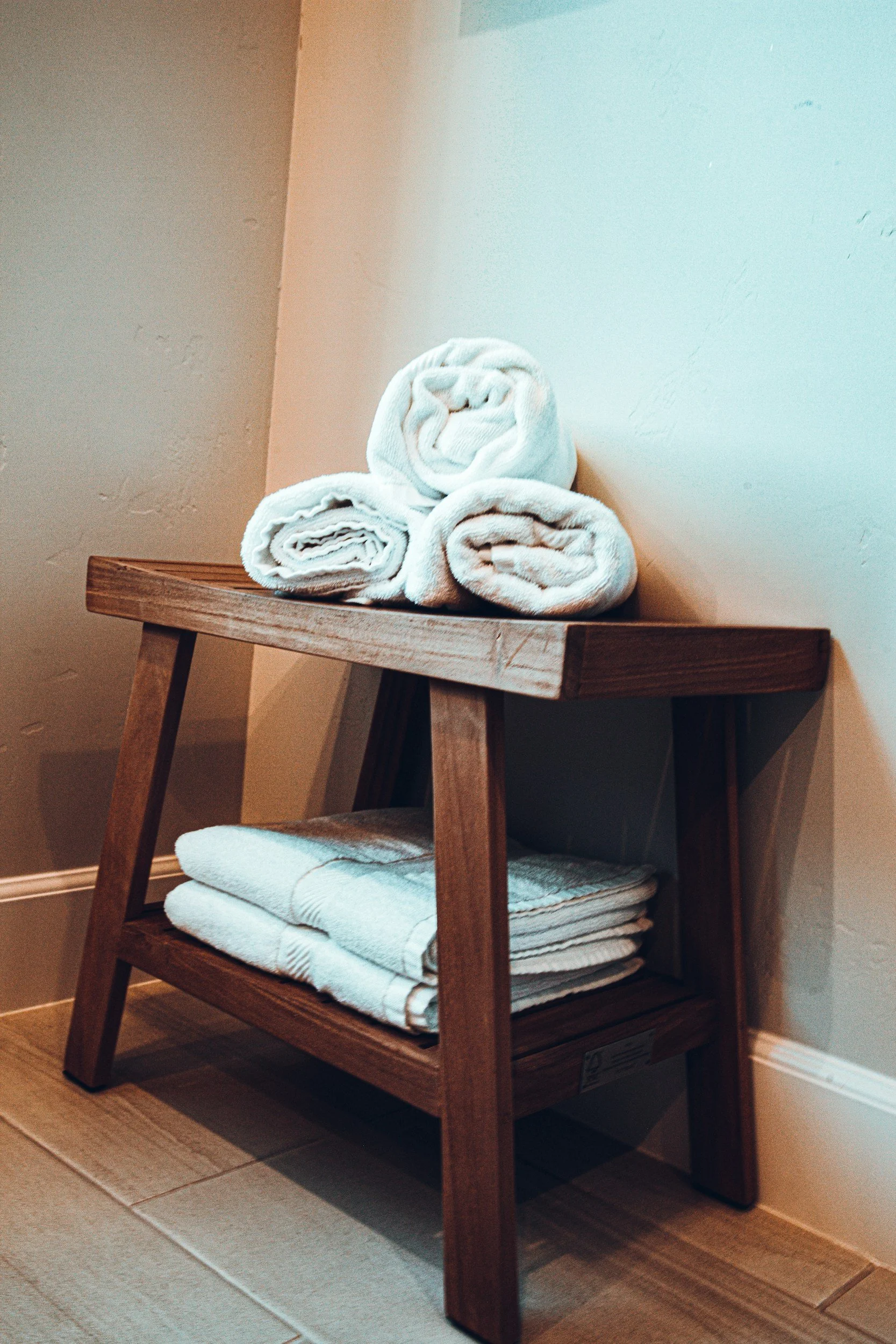 Stacked white towels on a wooden side table against a beige wall.