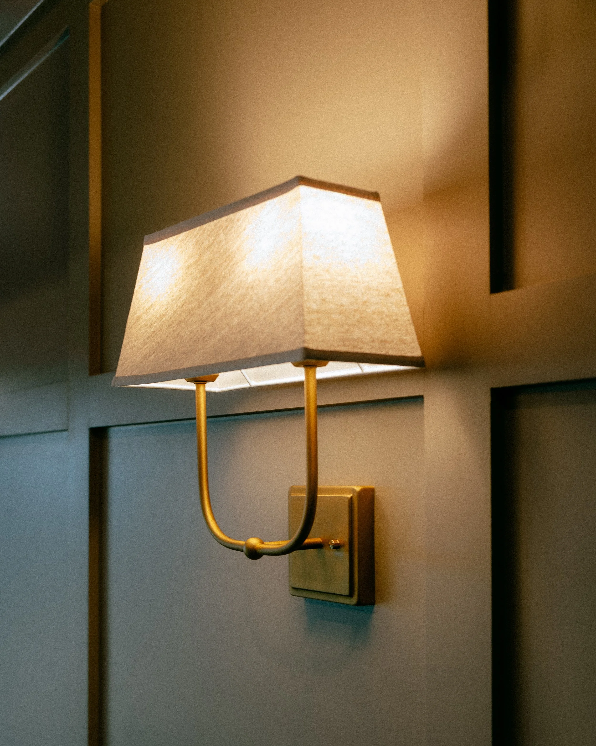 A wall-mounted sconce with a beige fabric shade emits light on a beige wall.