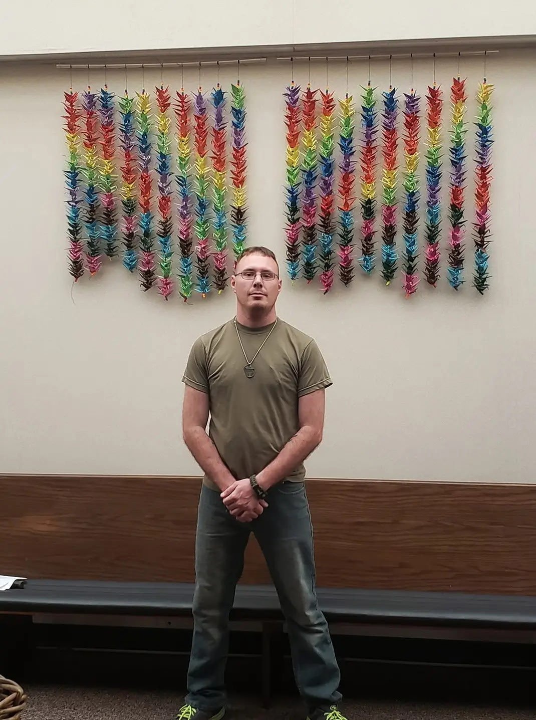 A man standing in front of a colorful origami crane display hanging on a wall.