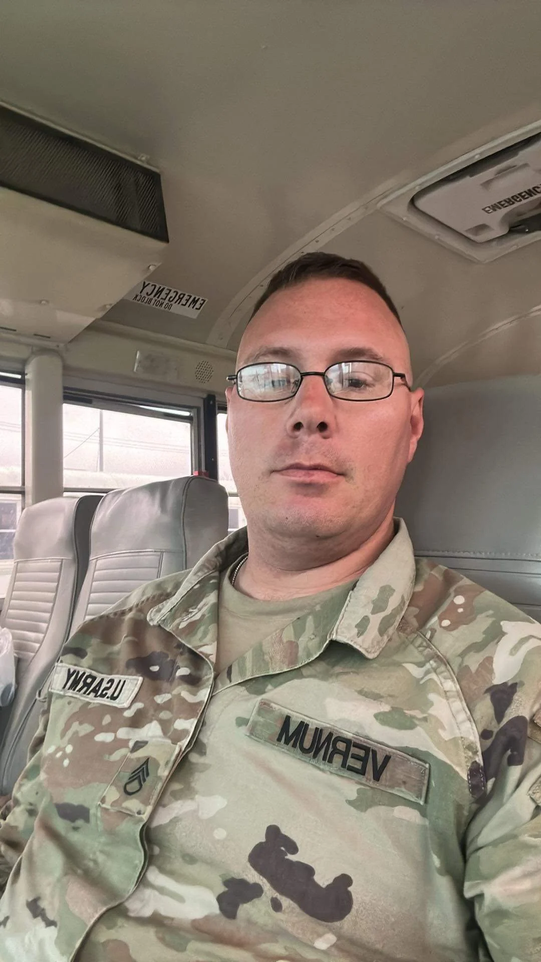 A man in military uniform with glasses sitting inside a vehicle.
