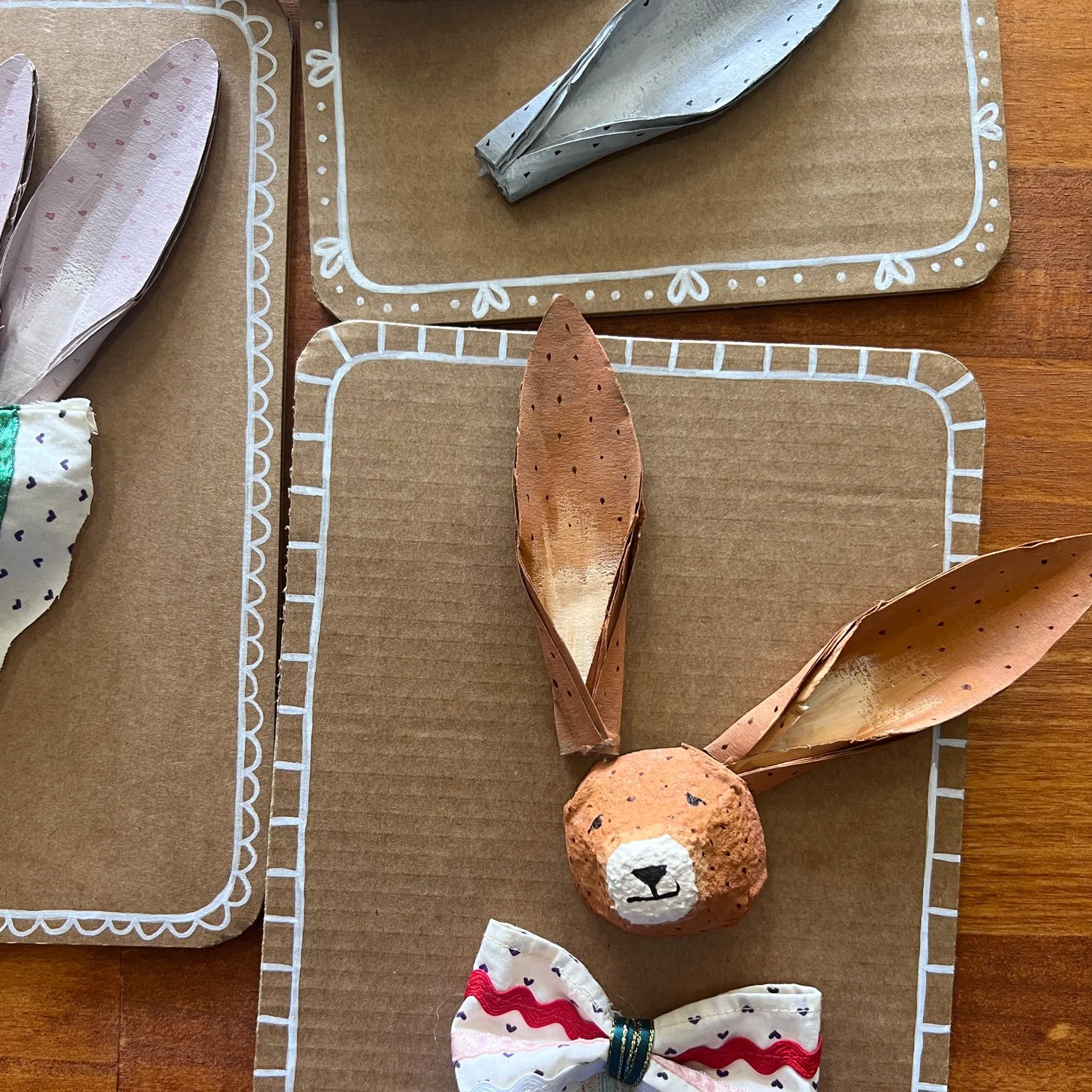 Materials for a children's craft workshop at Paper Caravan, including cardboard bunny shapes, colorful fabric ribbons, and paper collars ready for decorating.