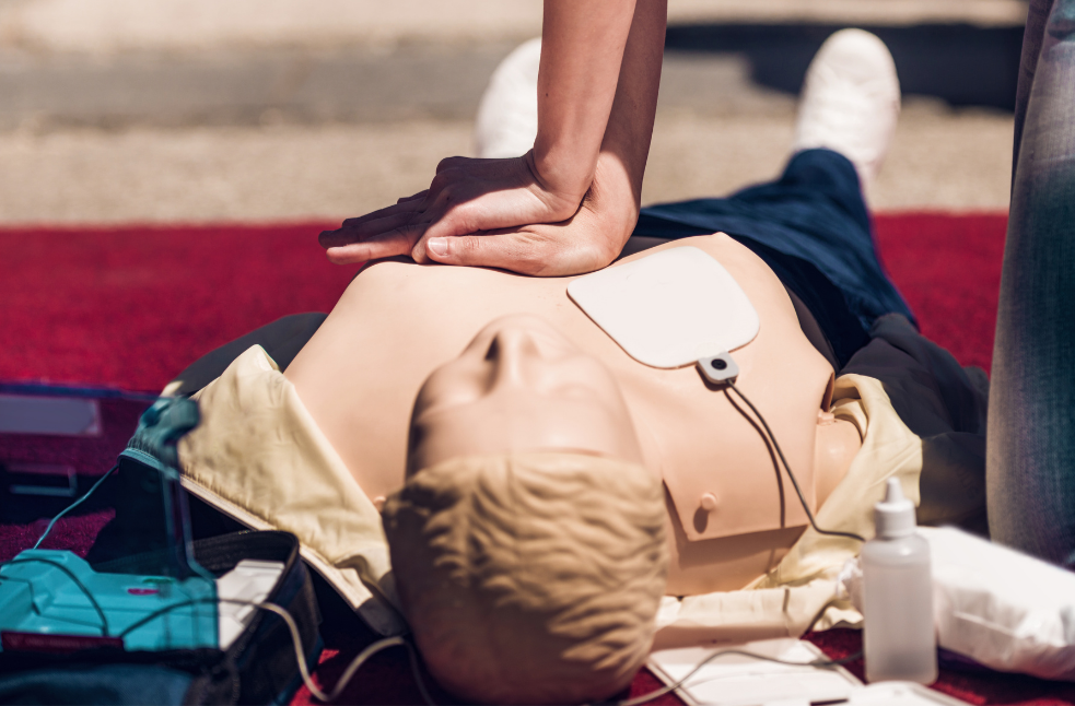 Person performing CPR on a training mannequin during a first aid demonstration outdoors.