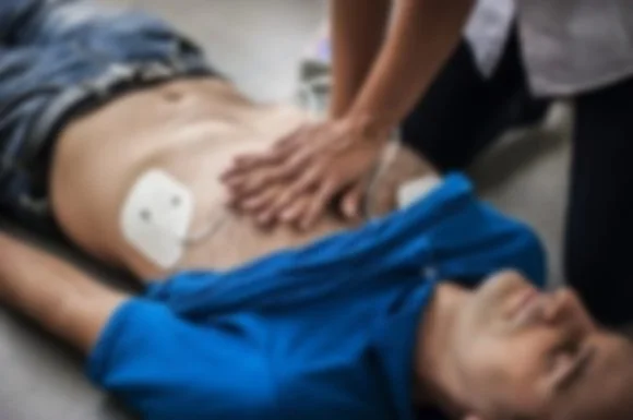 A person lying on their back receiving CPR, with a medical bandage on their abdomen and someone performing chest compressions.