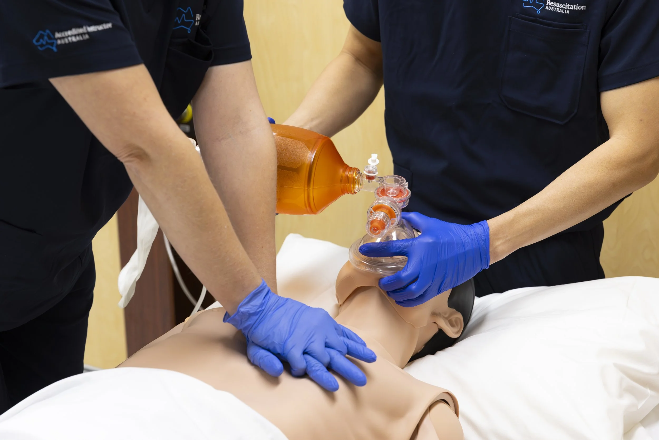 Medical professionals practicing CPR on a mannequin, with one administering rescue breaths using an oxygen mask and others supporting.