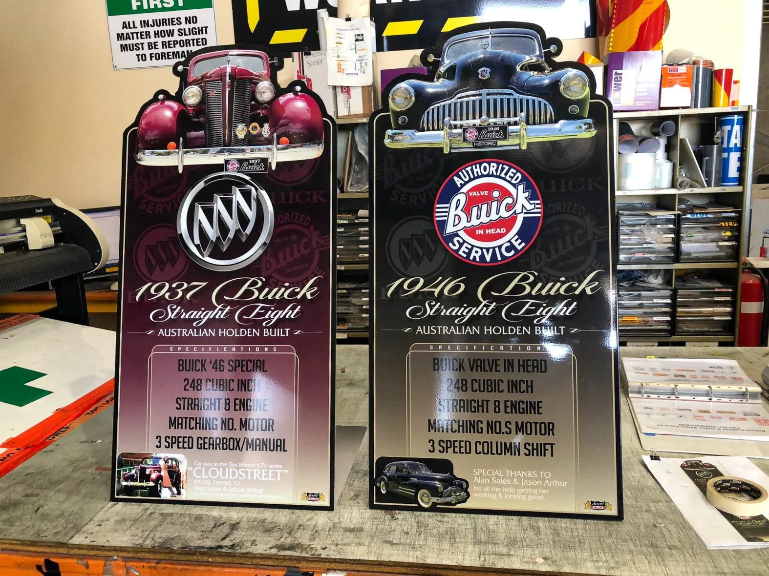 Two vintage car posters for 1937 Buick and 1946 Buick, displayed on a workbench with workshop tools and materials in the background.