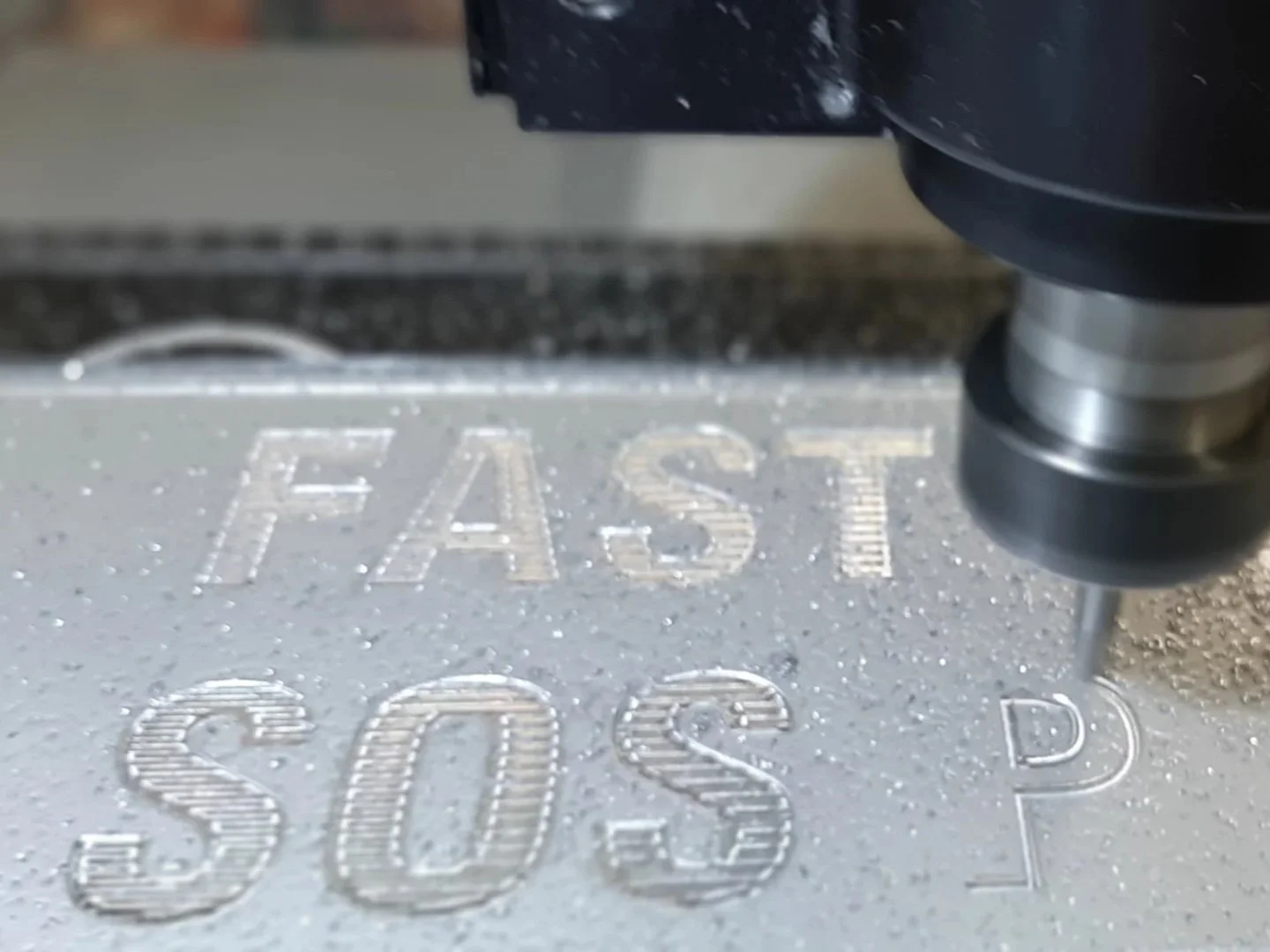 Close-up of a CNC machine engraving the words "FAST SOLID" onto a metallic surface with a tool creating tiny chips.