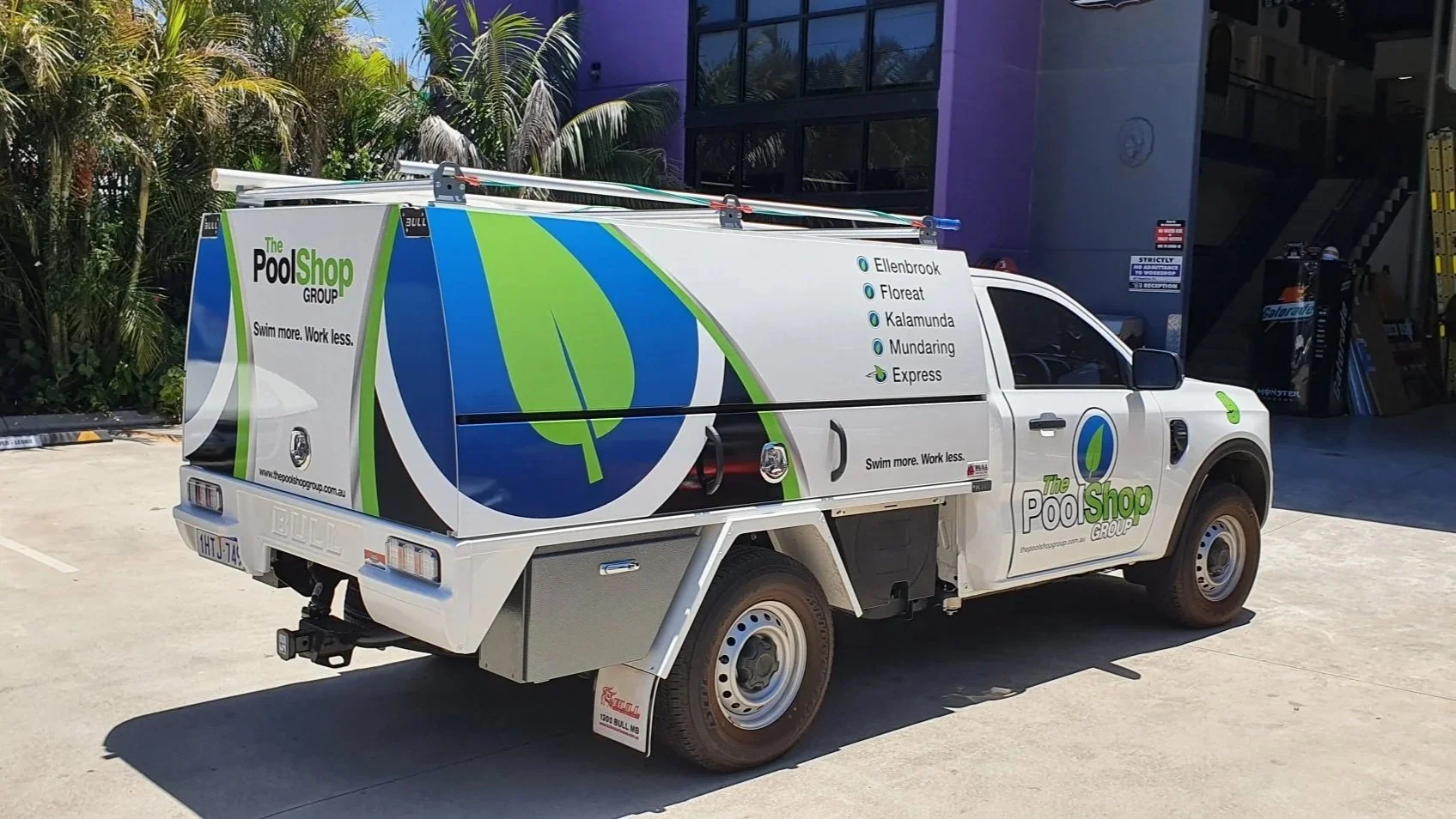 A white utility vehicle with branding for The Pool Shop Group, featuring a large logo of a green leaf and blue circle, parked on a concrete surface. The vehicle has advertisements for pool services with locations listed, and the slogan "Swim more. Work less."