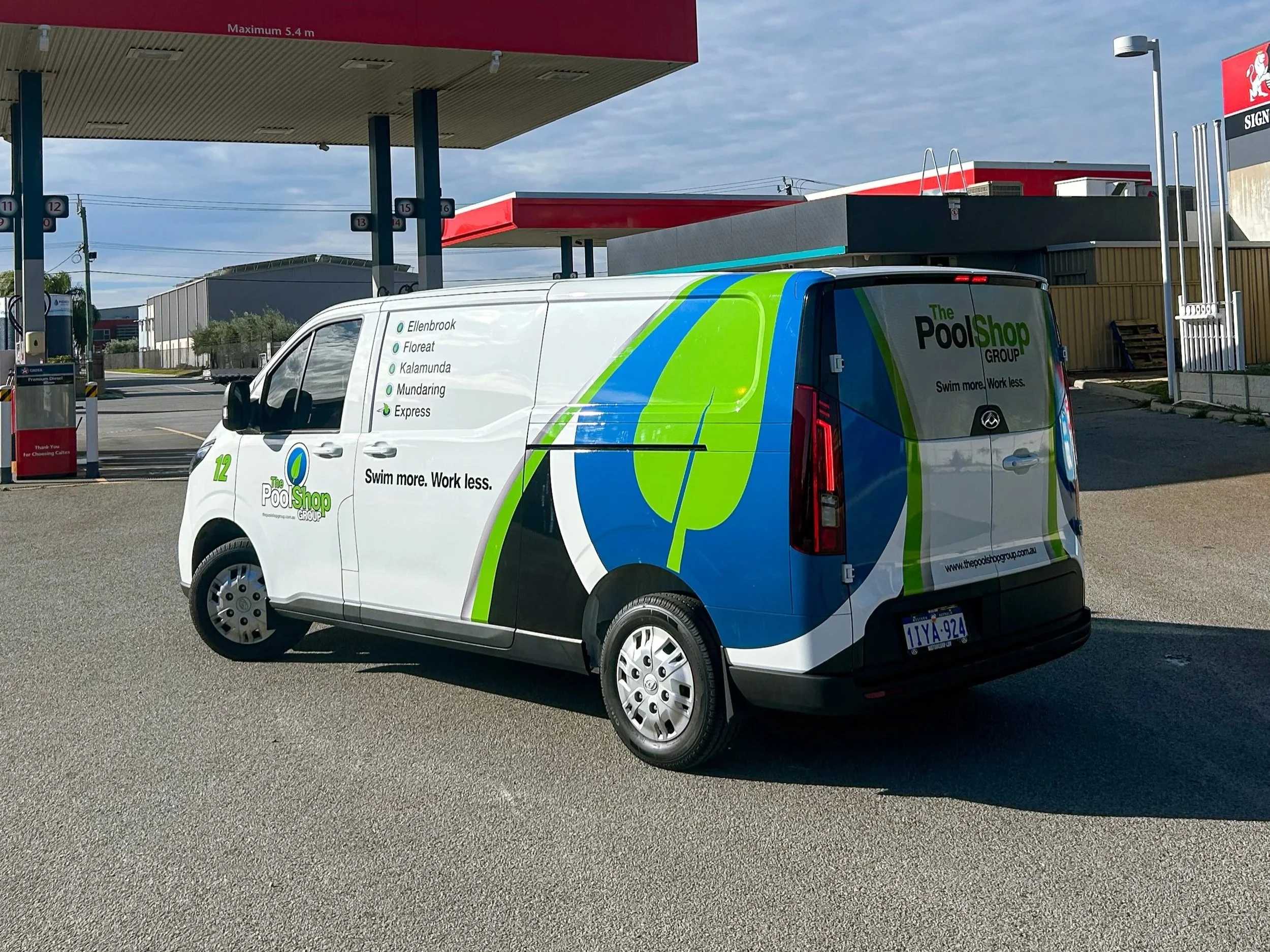 A white customer service van for The Pool Shop Group parked at a gas station, with the company’s logo and slogan 'Swim more. Work less.' on the side. The gas station canopy and pumps are visible in the background.