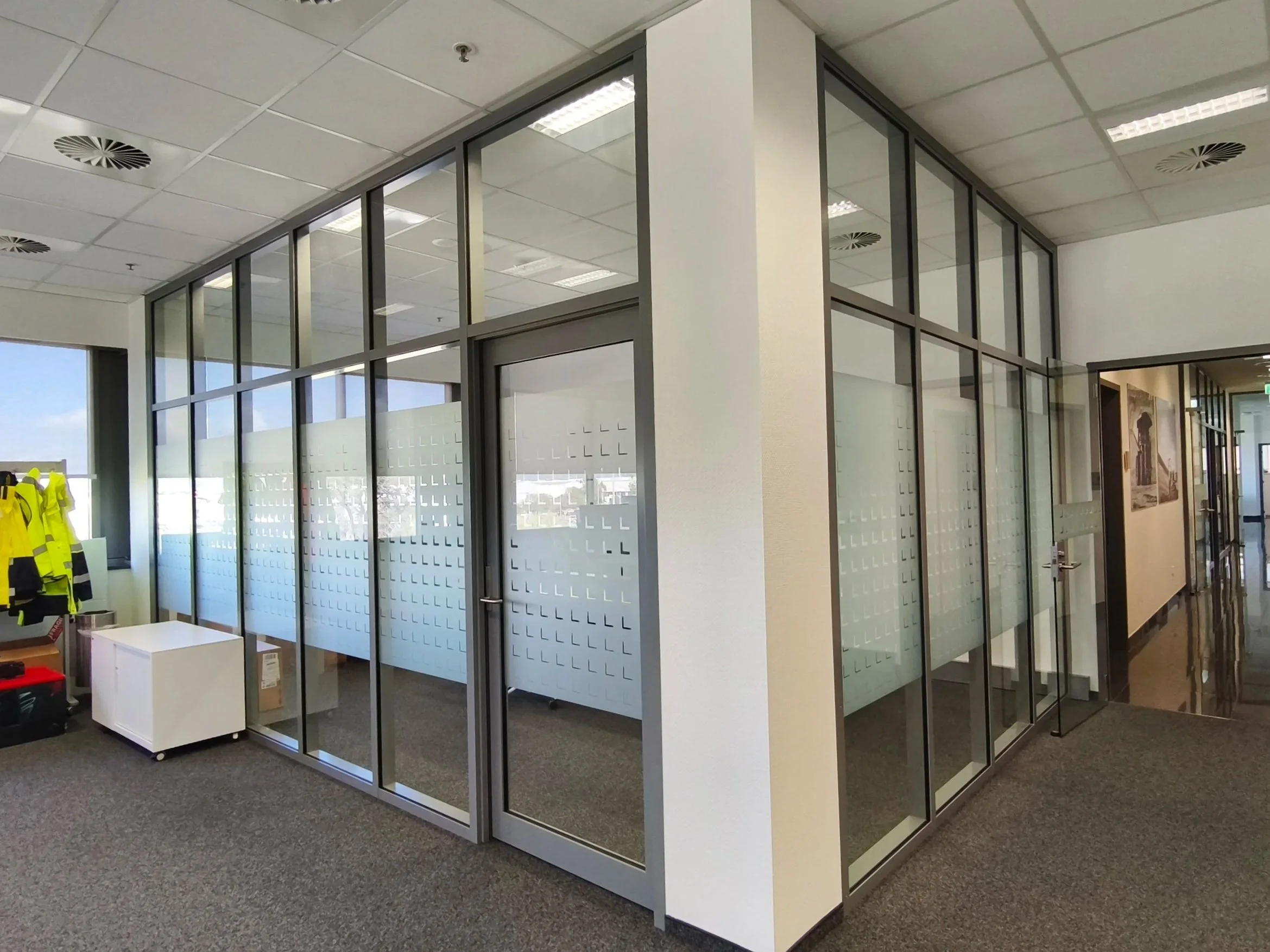 Office cubicle with frosted vinyl glass walls, located in a professional workspace, with a white cabinet, some yellow safety vests, and office supplies nearby. Office signage. Privacy signage