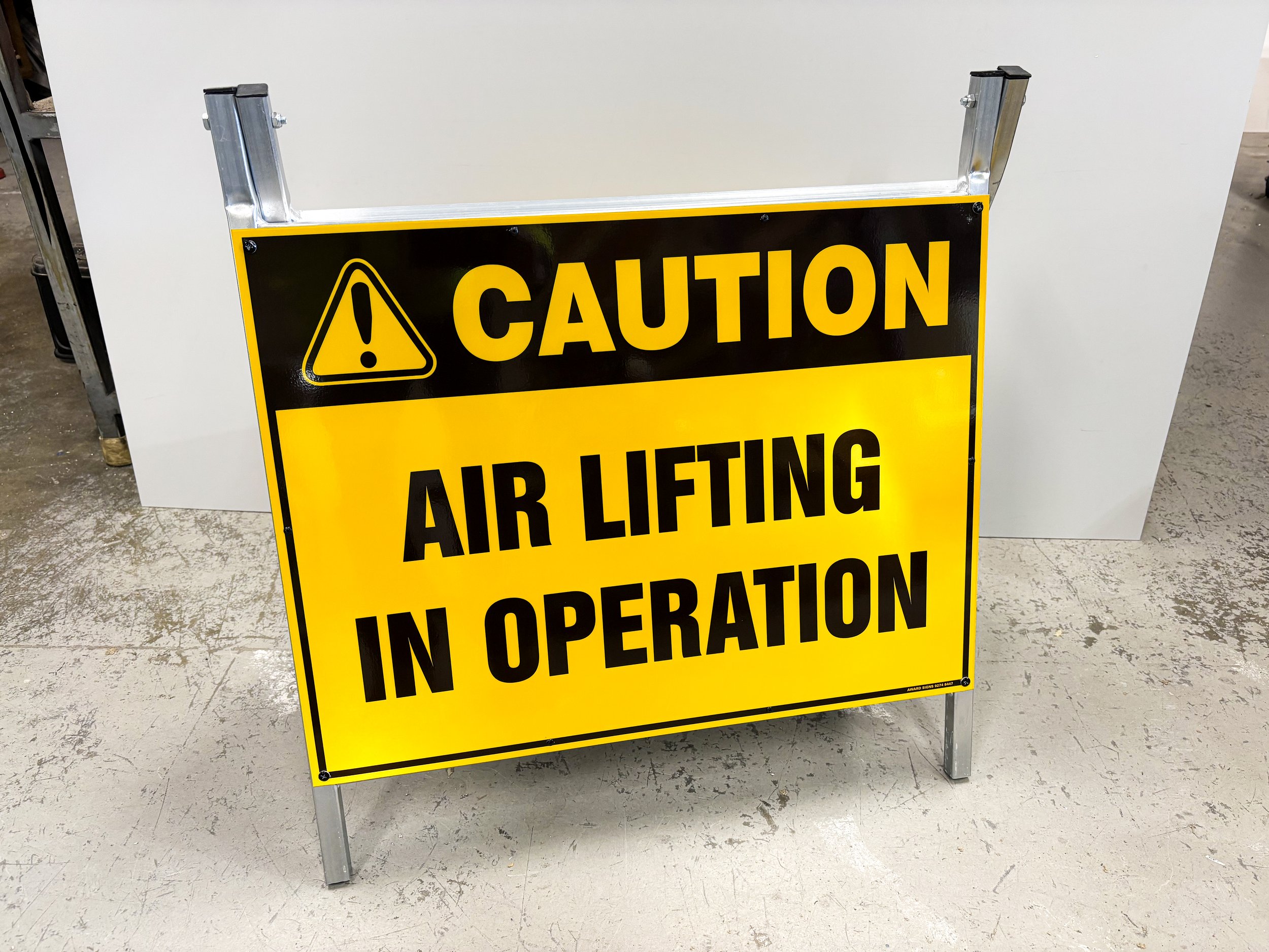 A yellow and black caution sign on a stand indicating air lifting operation in progress. Custom A-Frame Signage. Perth Signage. Portable Sign. High Visibility Sign. Safety Sign. Western Australia Sign. Mining Signage. 