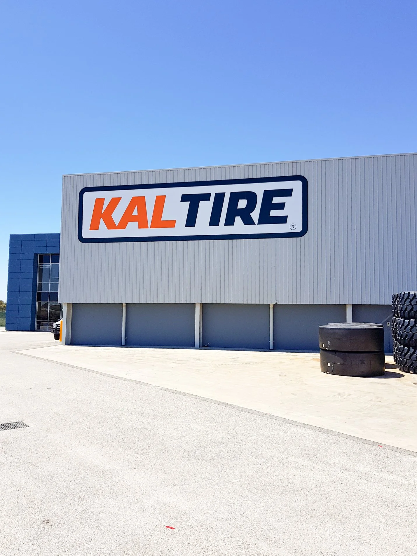 Exterior view of a tire store with a large sign reading 'KAL TIRE' on the building. There are some tires stacked outside the building. Business branding and business signage