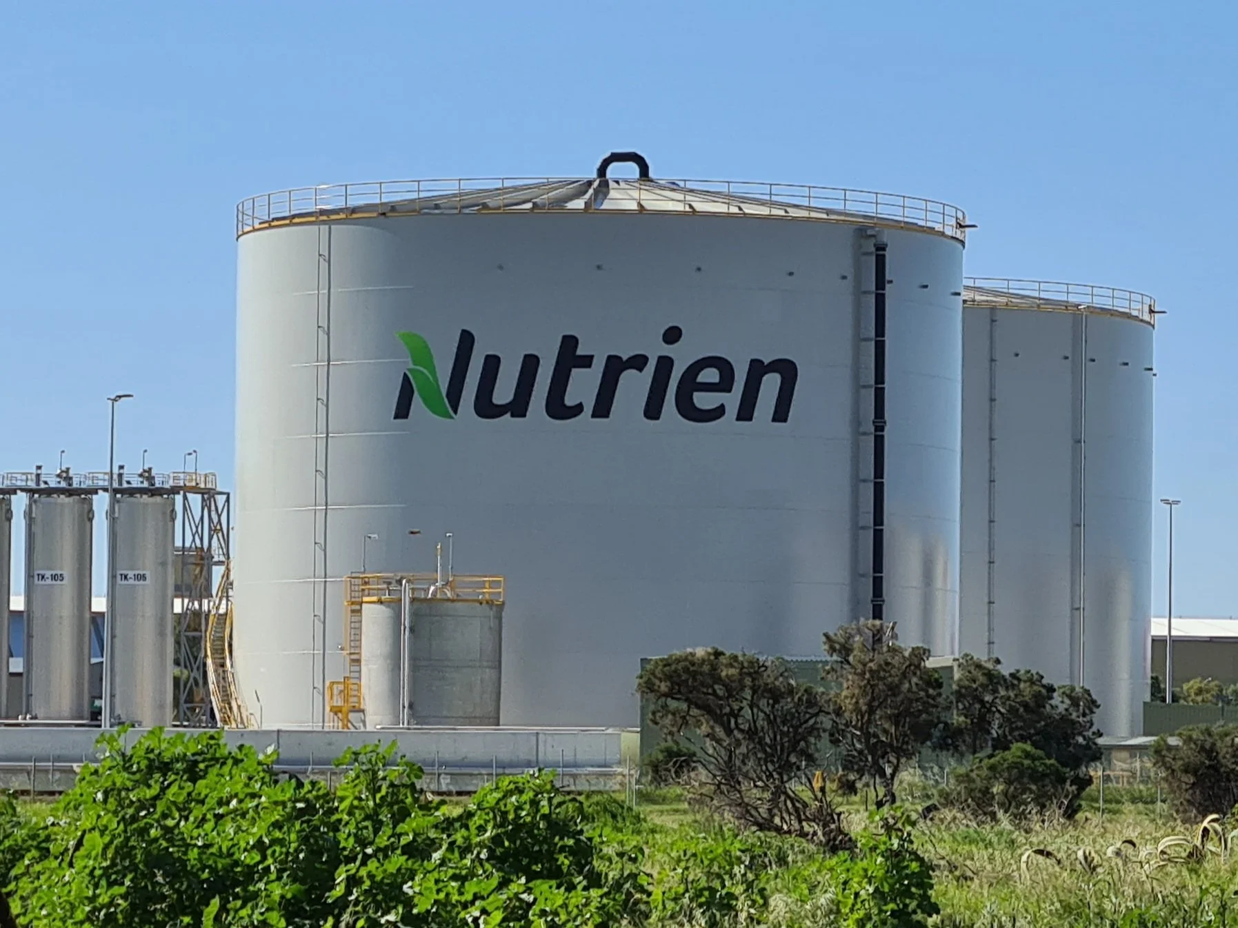 Large agricultural storage silos with painted 'Nutrien' logo in an industrial area.