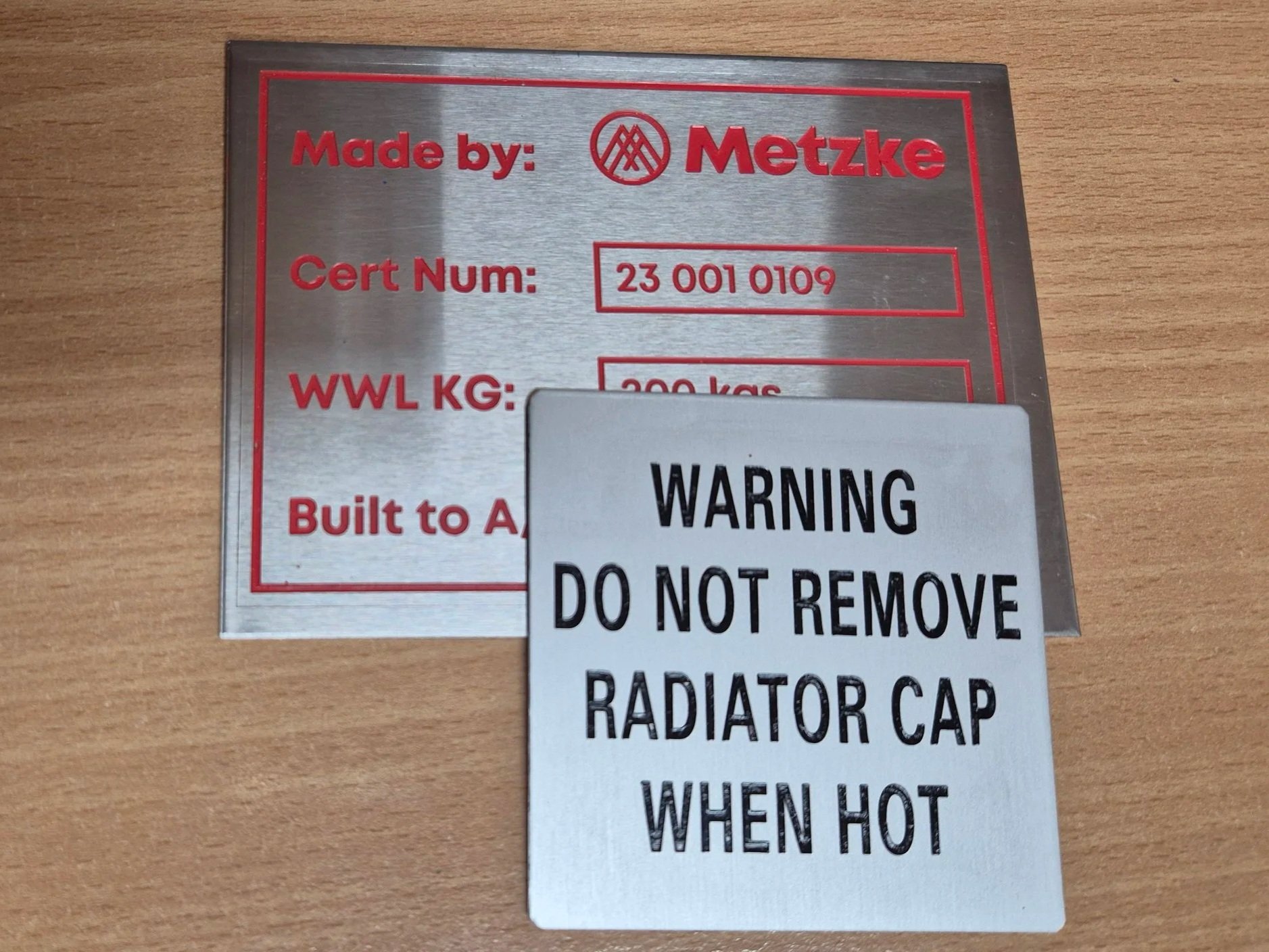Engraved Metal identification plate with filled red text displaying manufacturer, certification number, and weight capacity, with a white warning label. Safety decals and tags