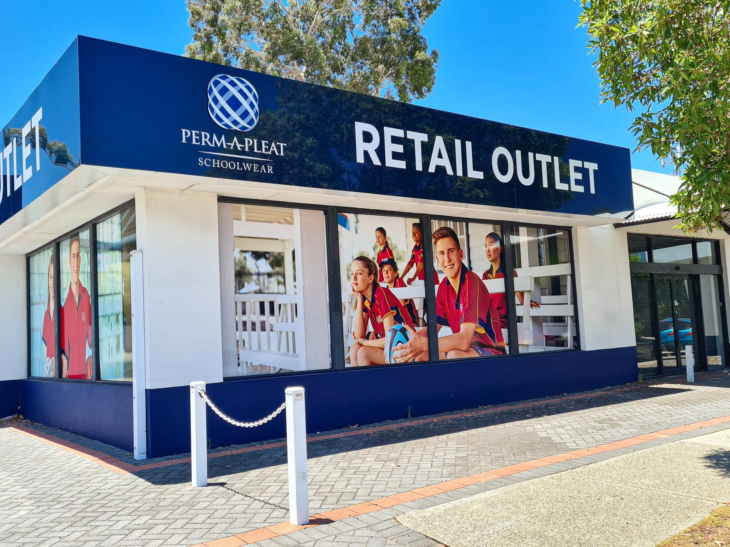 Sign for PERMA-PLEAT SCHOOLWEAR Retail Outlet with images of children in sports uniforms on windows. Business Signage
