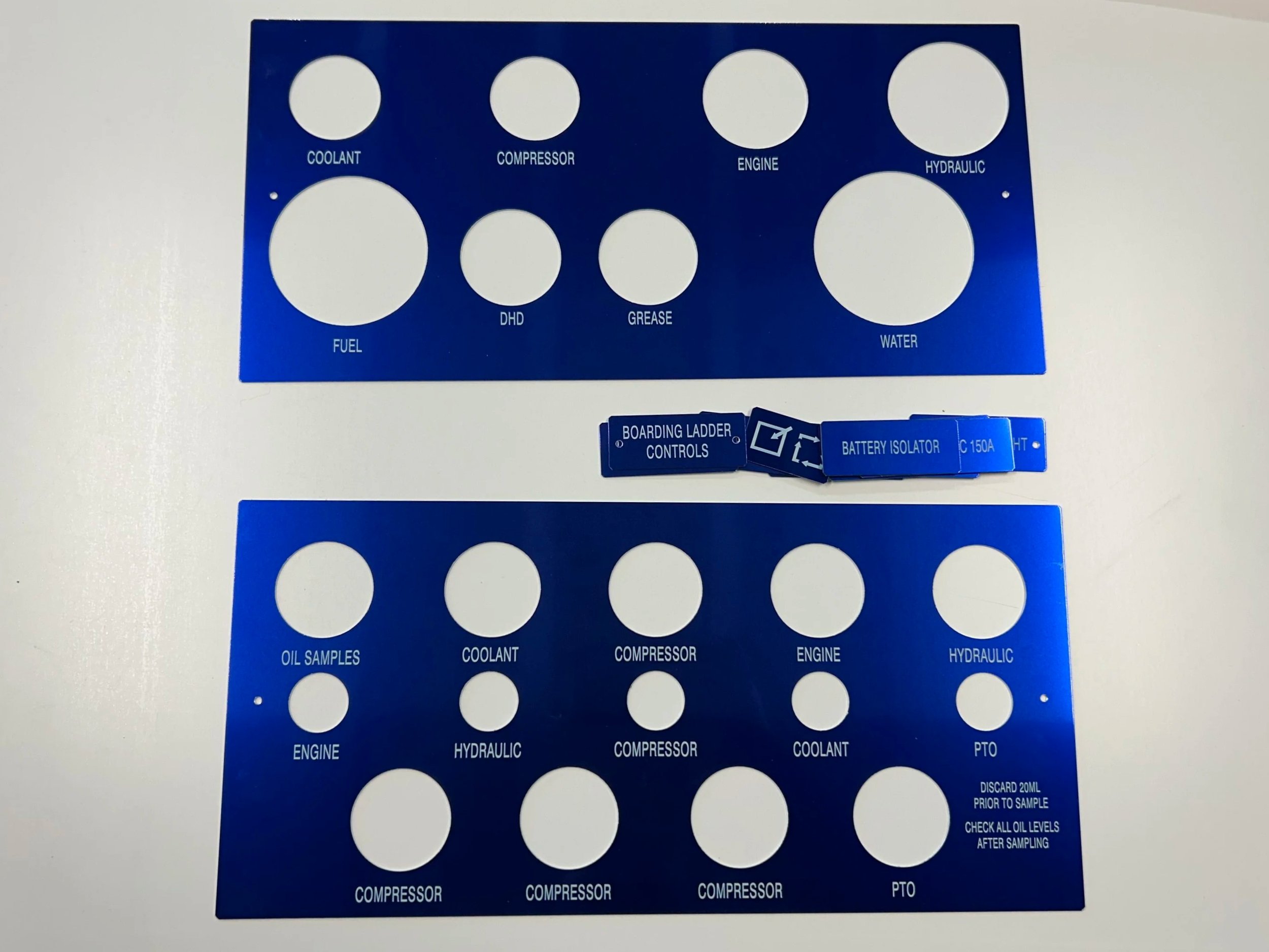 Blue circular stencil template with labeled cutouts for vehicle engine parts and fluids, including coolant, compressor, engine, hydraulic, fuel, DHD, grease, water, oil samples, and PTO.
