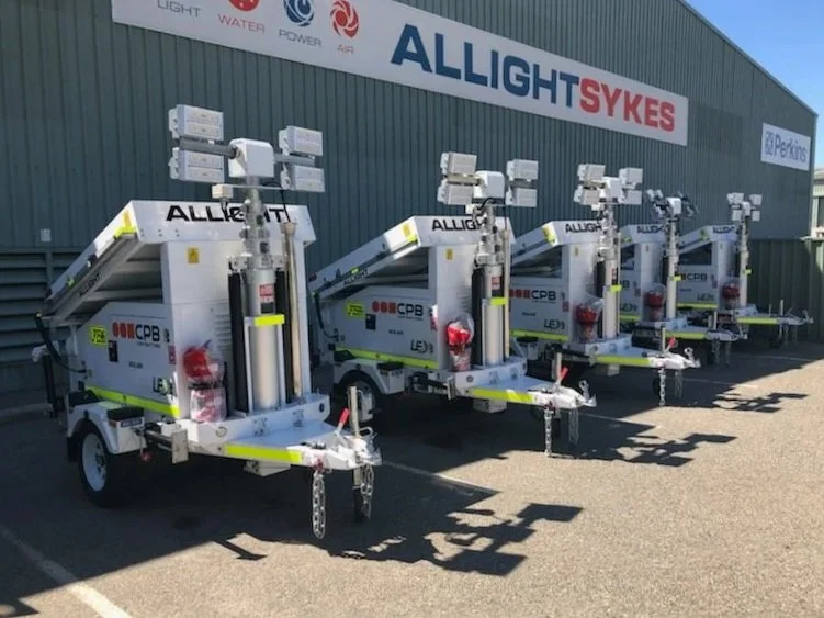 Five mobile elevated work platforms lined up outside a building with a sign reading 'ALLIGHT SYKES.' Commercial vehicle signage