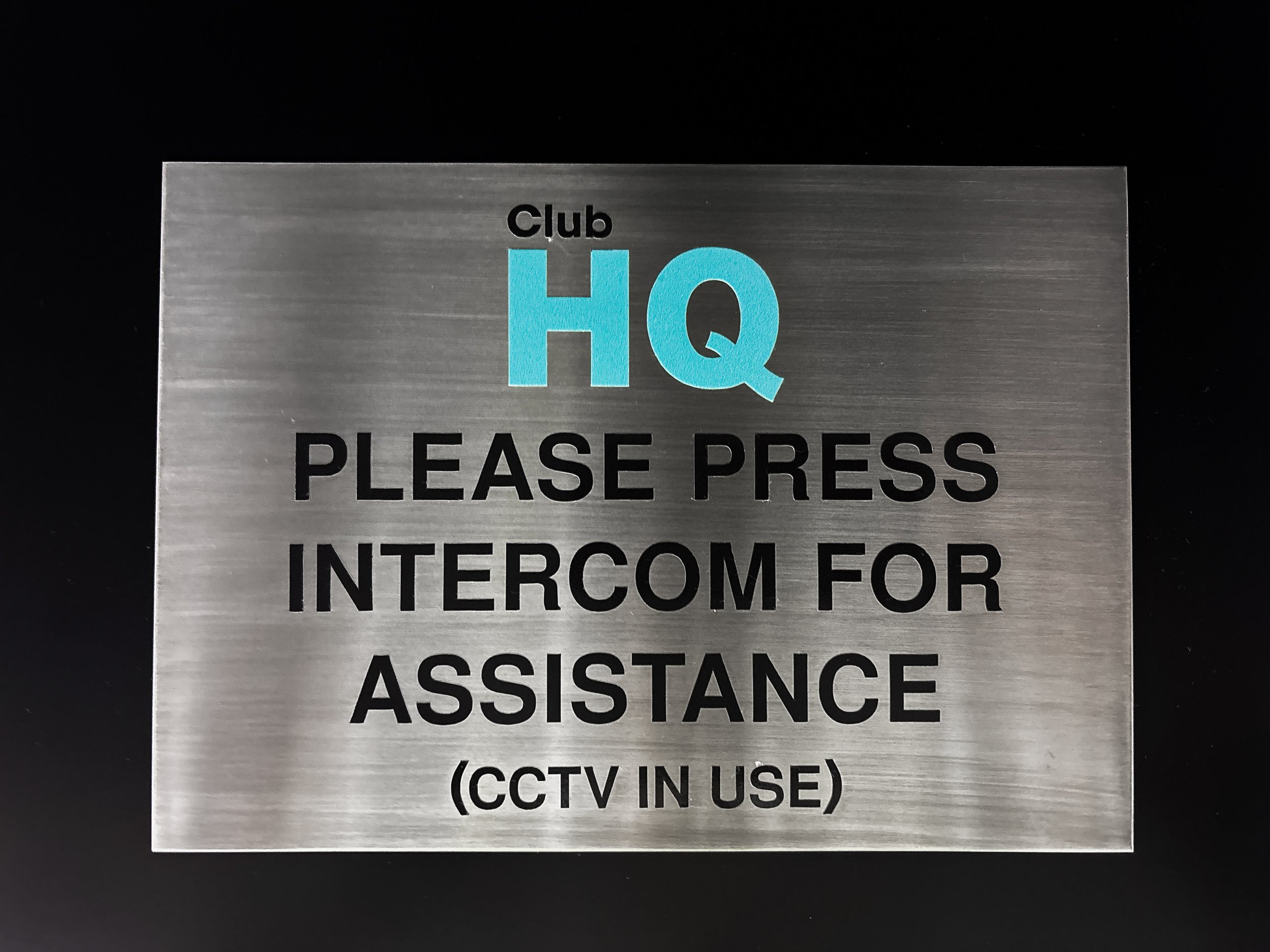 Small brushed metal sign indicating the entrance to a childcare club, requesting visitors to press for intercom assistance, with mention of CCTV in use. Custom signage Perth. Custom Brushed Aluminium Sign Perth. Custom Metal Entrance Signs Perth.