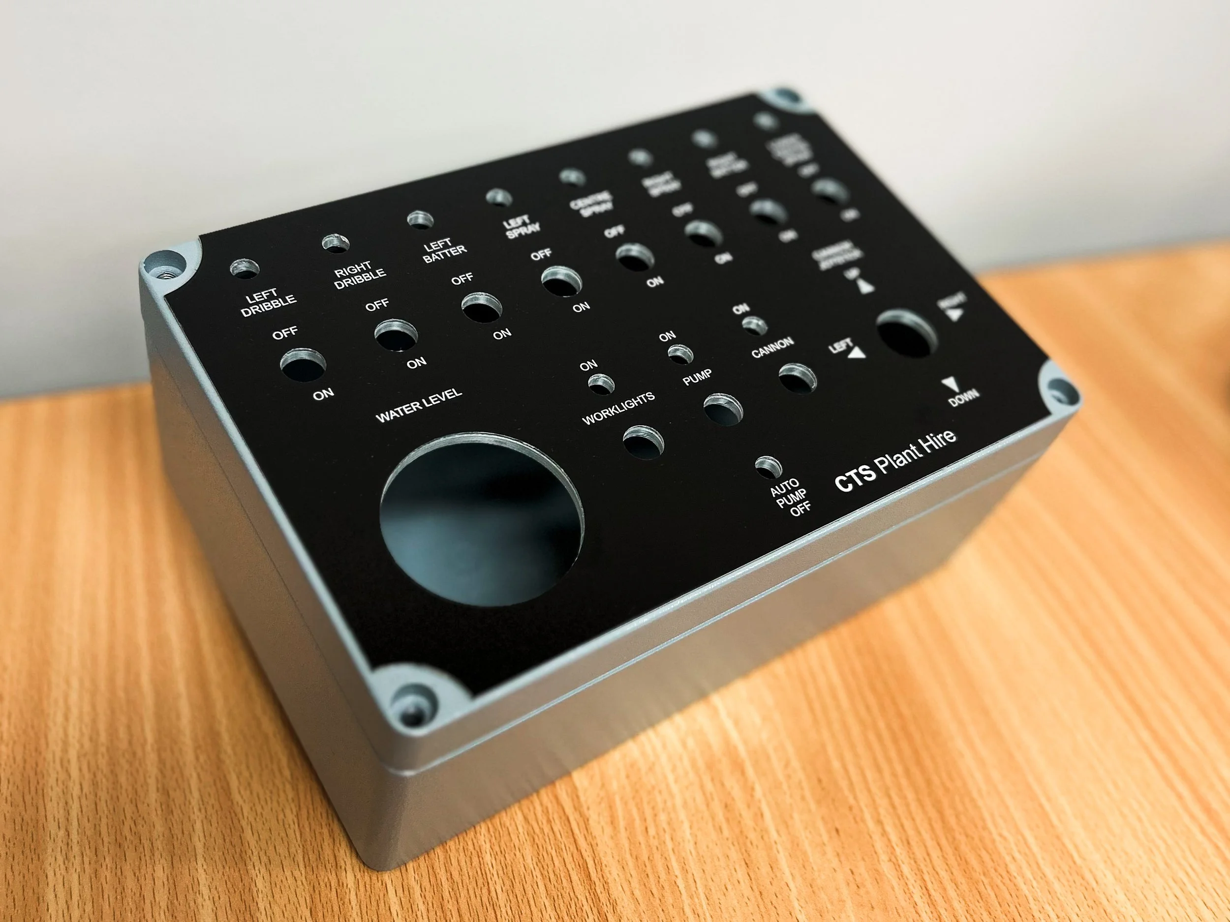 A black metal panel with multiple labeled holes for switches and connectors is placed on a wooden surface.
