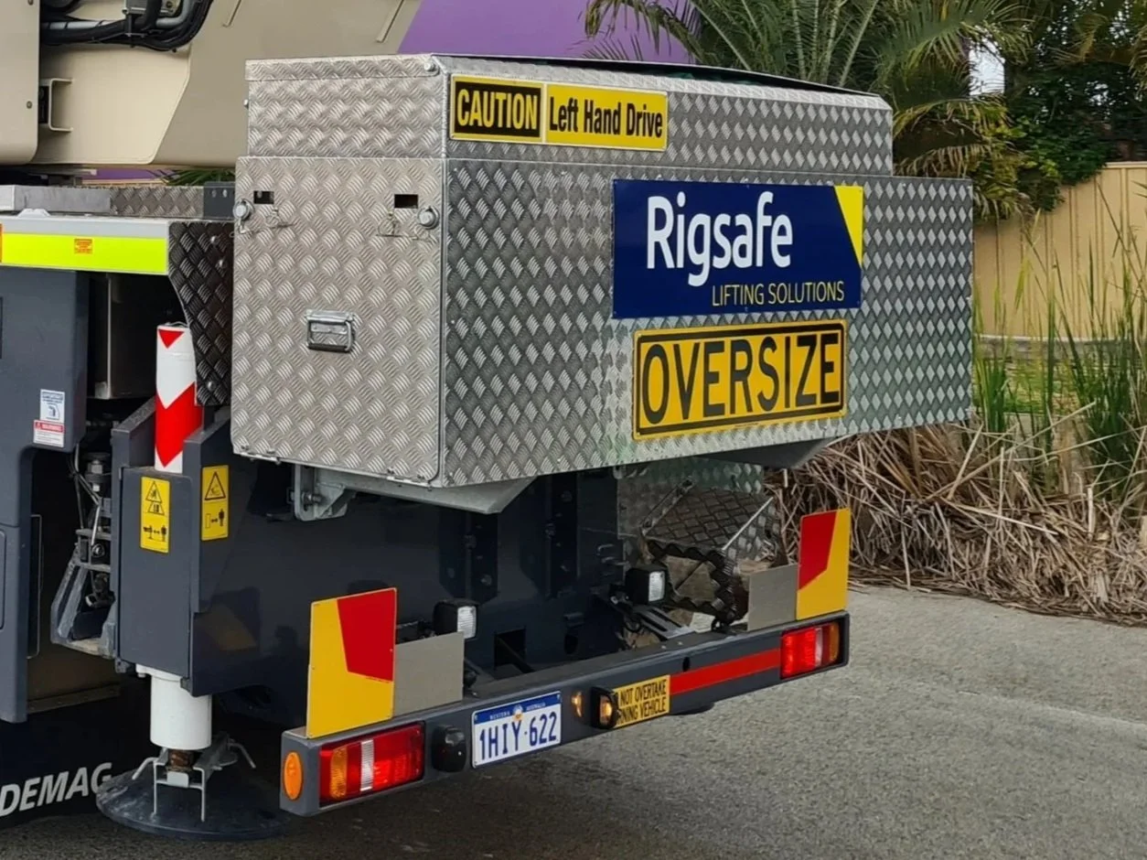 Utility vehicle with diamond-plate storage box displaying signage that reads "Caution Left Hand Drive," "Rigsafe Lifting Solutions," and "Oversize" in yellow and black, along with reflective red and yellow safety markings. Regulatory Road Signage