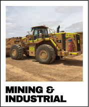 A large yellow and black construction vehicle working on a dirt construction site with a cloudy sky overhead.