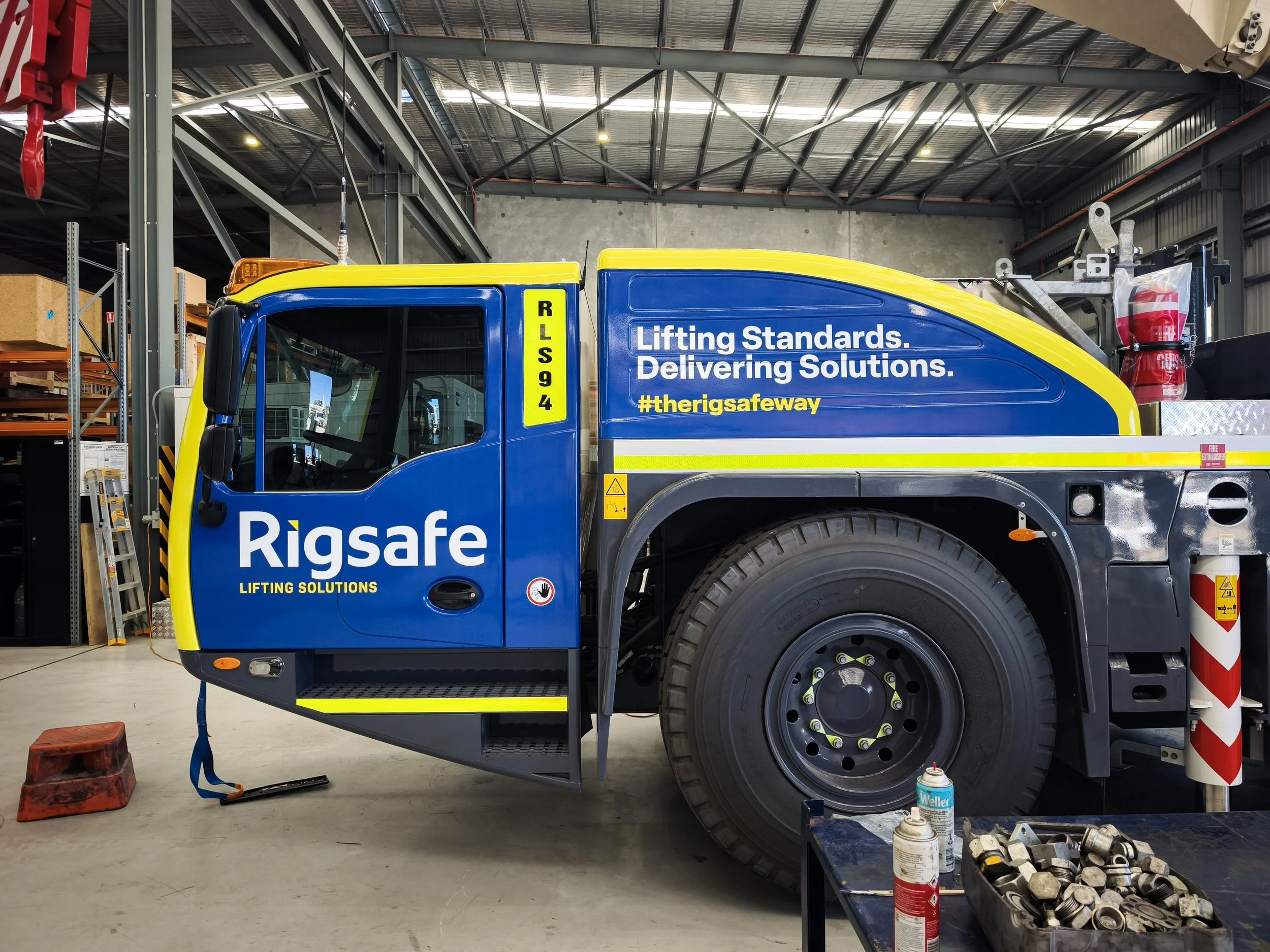 A rescue truck inside a warehouse or garage, labeled with 'RLS94' and 'Rigsafe', with safety equipment, fire extinguisher, and cleaning supplies nearby.