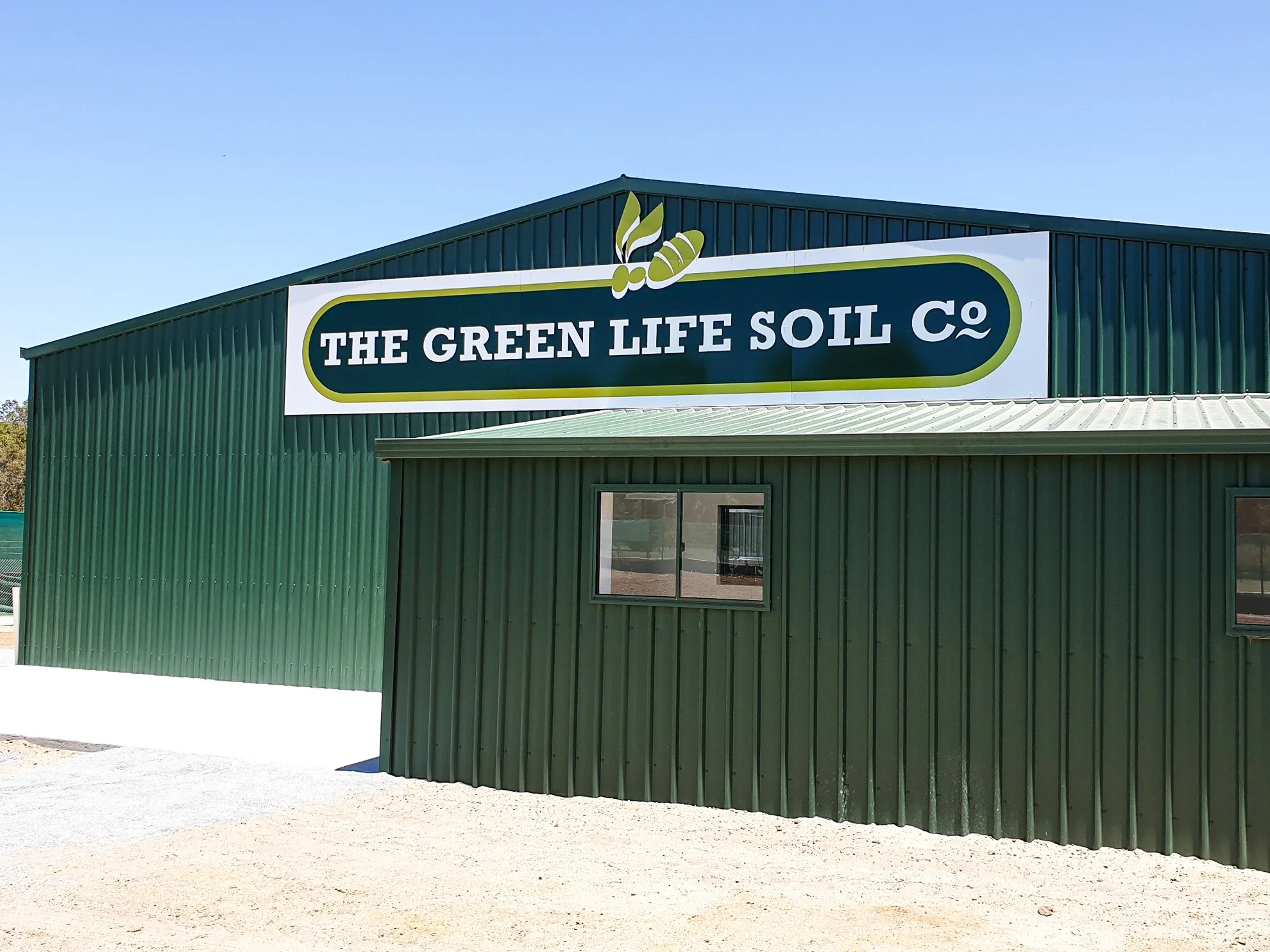 Green building with a large sign reading 'The Green Life Soil Co' and logo of a leaf and a root. Fascia Business Signage
