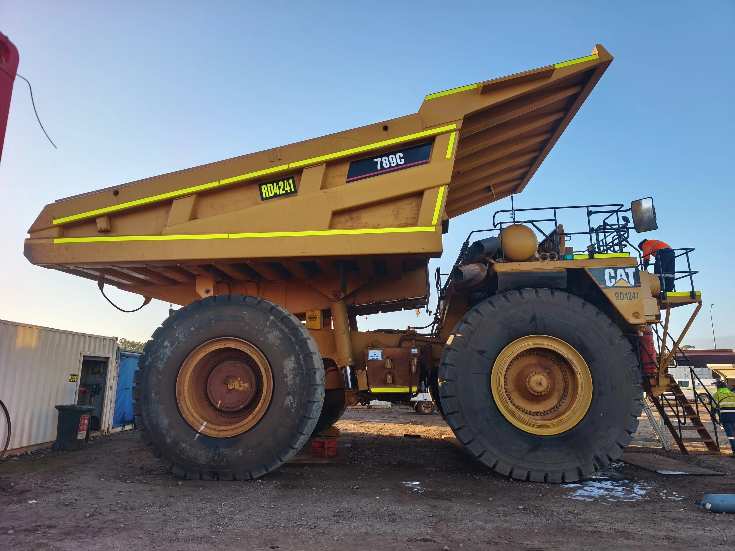 A large yellow Caterpillar dump truck with a raised bed at a working site. Mining machinery safety high visibility DG3 decals