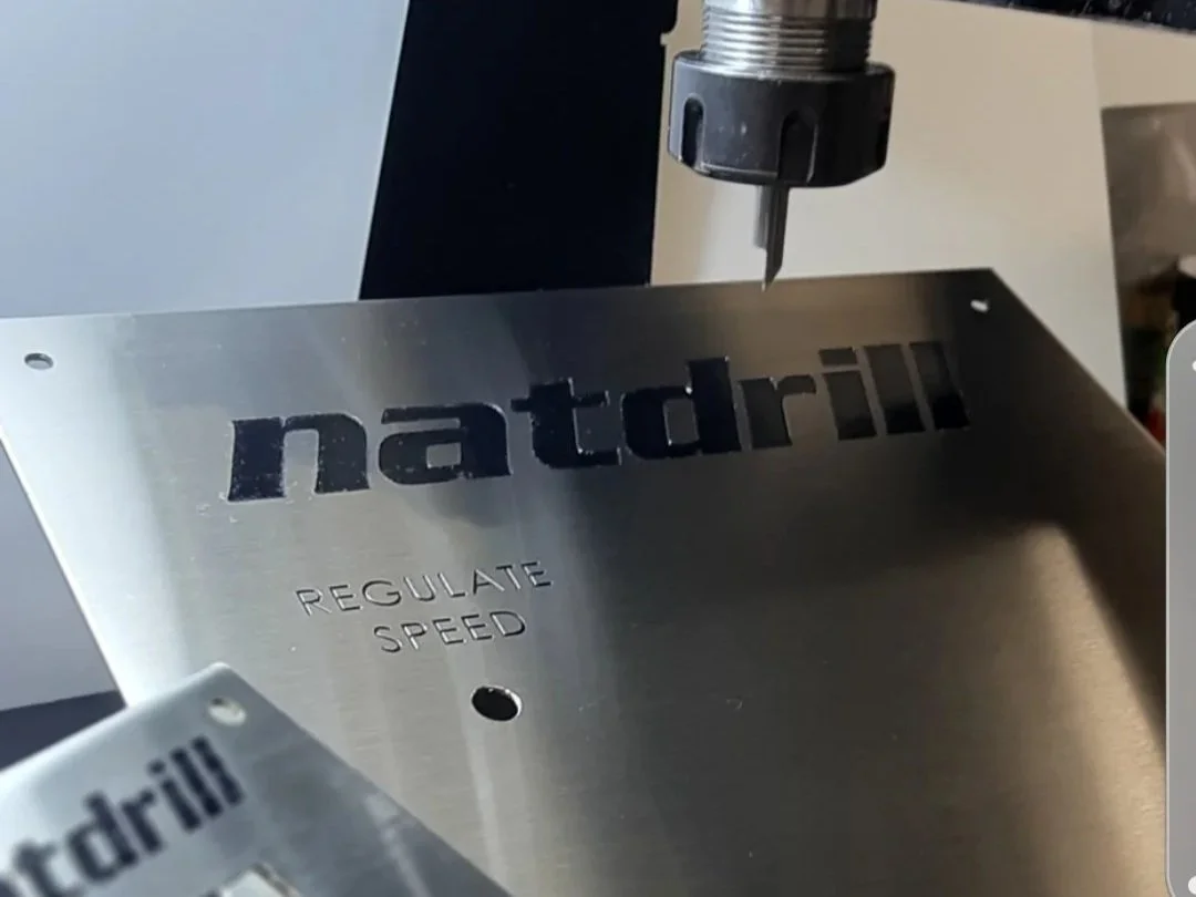 A metal machine part with the word 'natrill' engraved on it, and a small section carved to say 'REGULATE SPEED', with a drill bit above it.