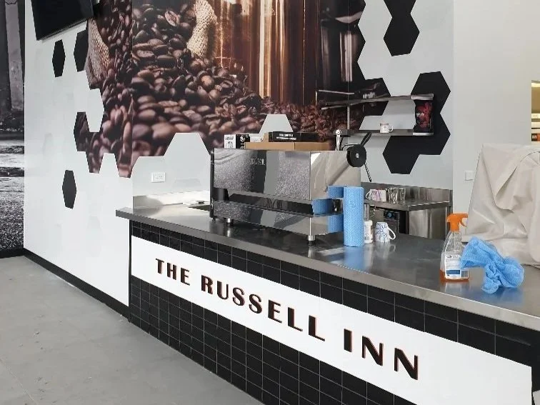 Coffee counter in a hotel lobby with a large coffee-themed mural and a sign reading 'The Russell Inn'. Business Hospitality Signage