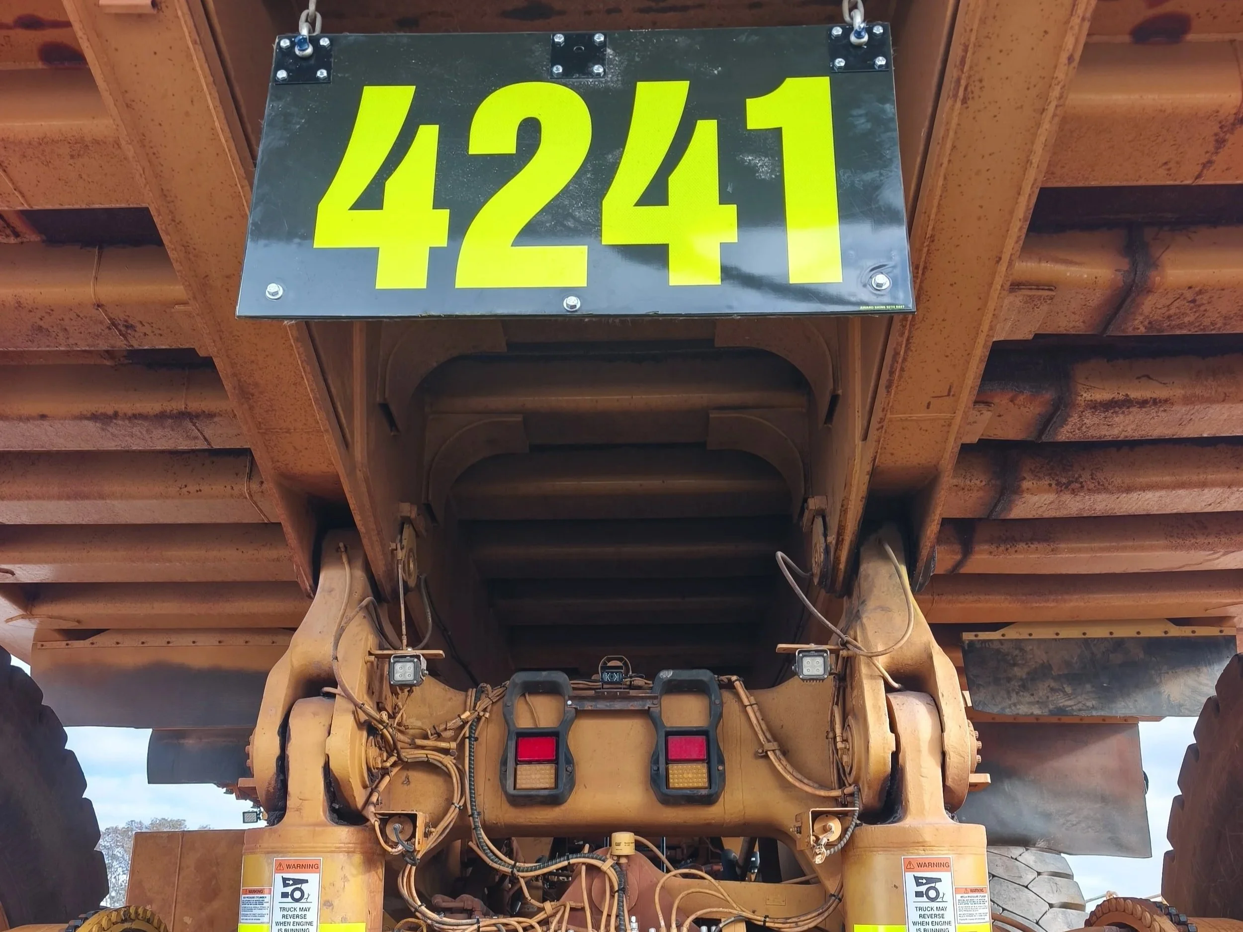 The image shows the rear view of a large, yellow construction vehicle, possibly a bulldozer or an excavator, with a black hanging sign displaying the numbers '4241' in bright yellow.