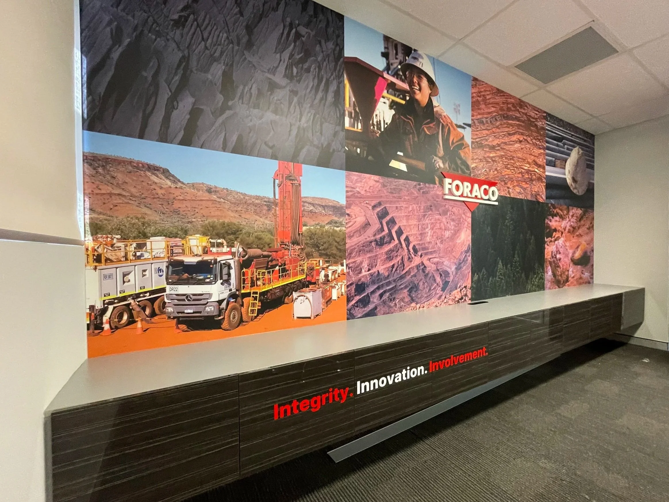 A mural on a wall featuring a firefighter with a helmet, construction scenes, rocky landscapes, and the words 'Integrity. Innovation. Involvement.' Meeting room signage
