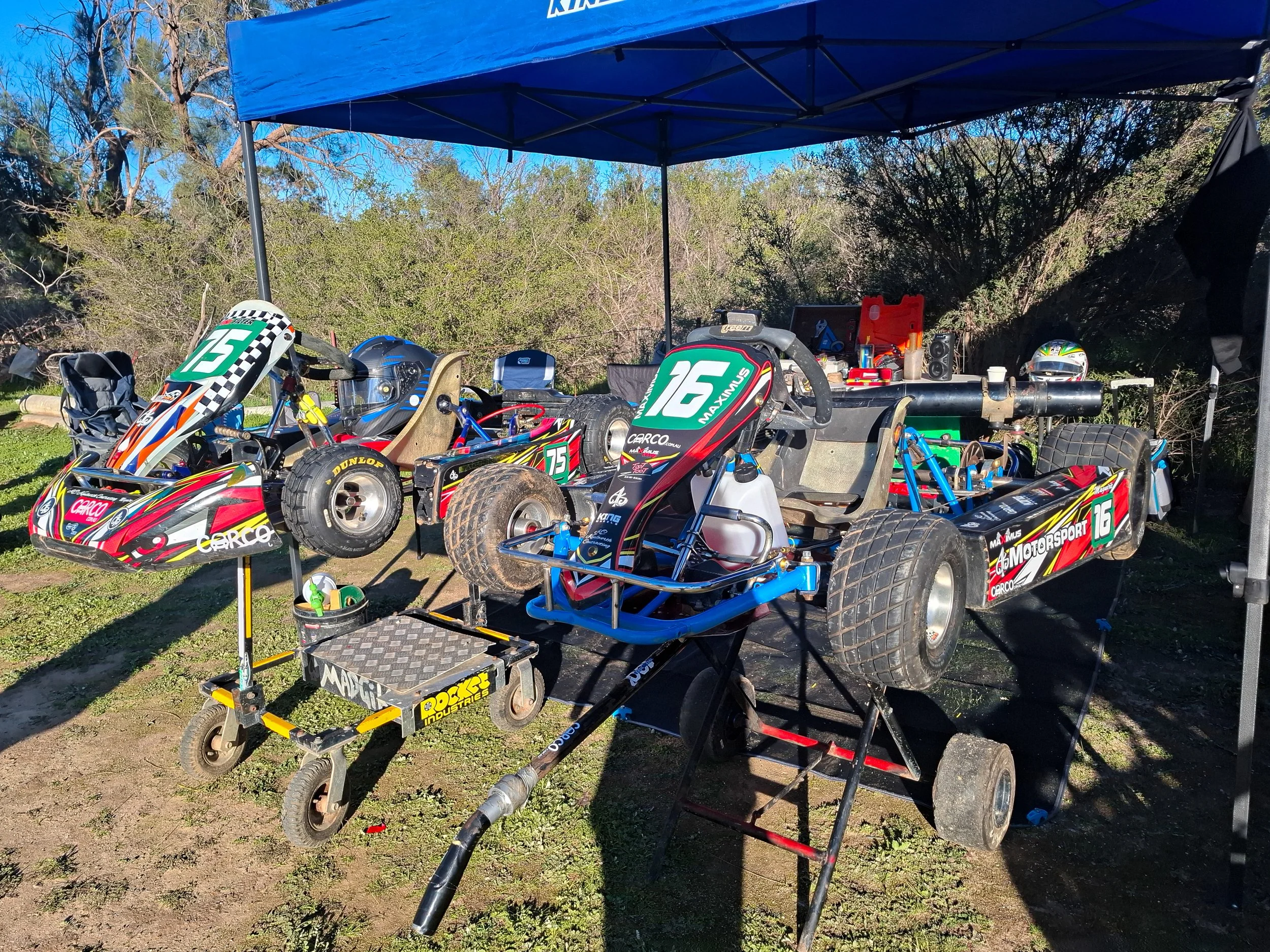 Two racing go-karts at the track with racing numbers and motorsport sponsor decals.