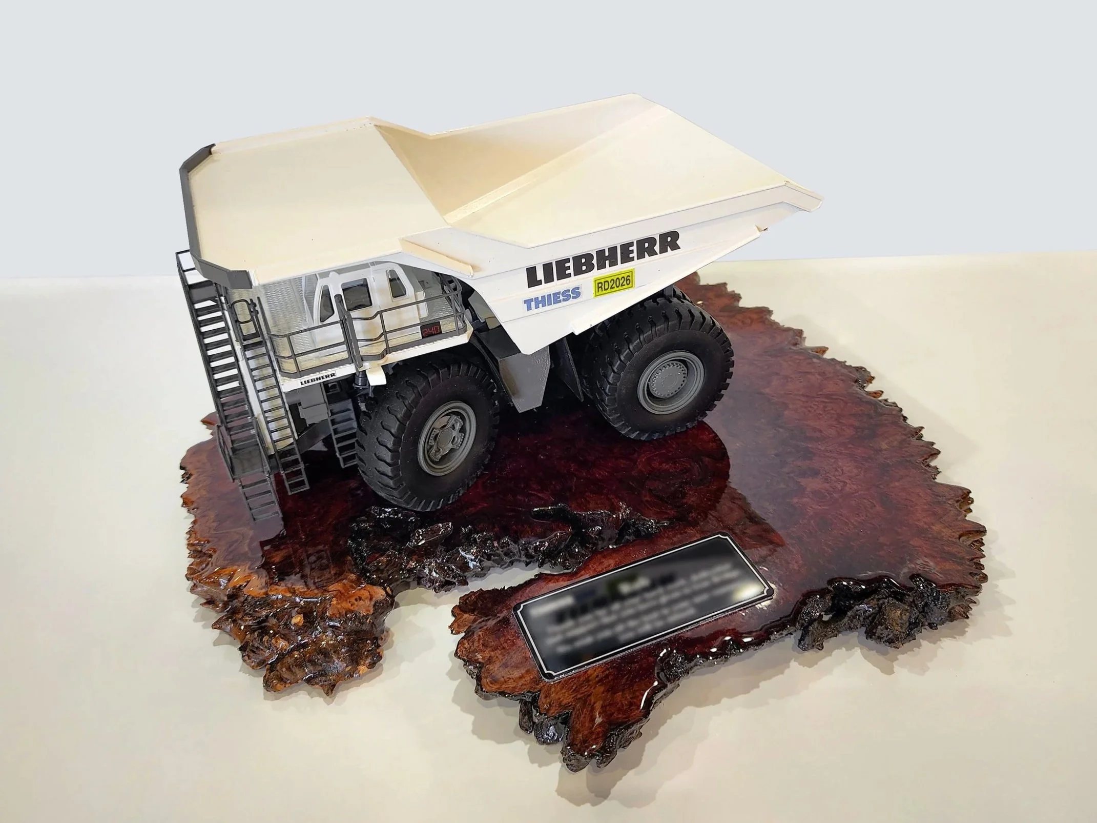 A detailed model of a Liebherr excavator displayed on a polished wooden base with a plaque, shown from a side angle. Custom mining gifts
