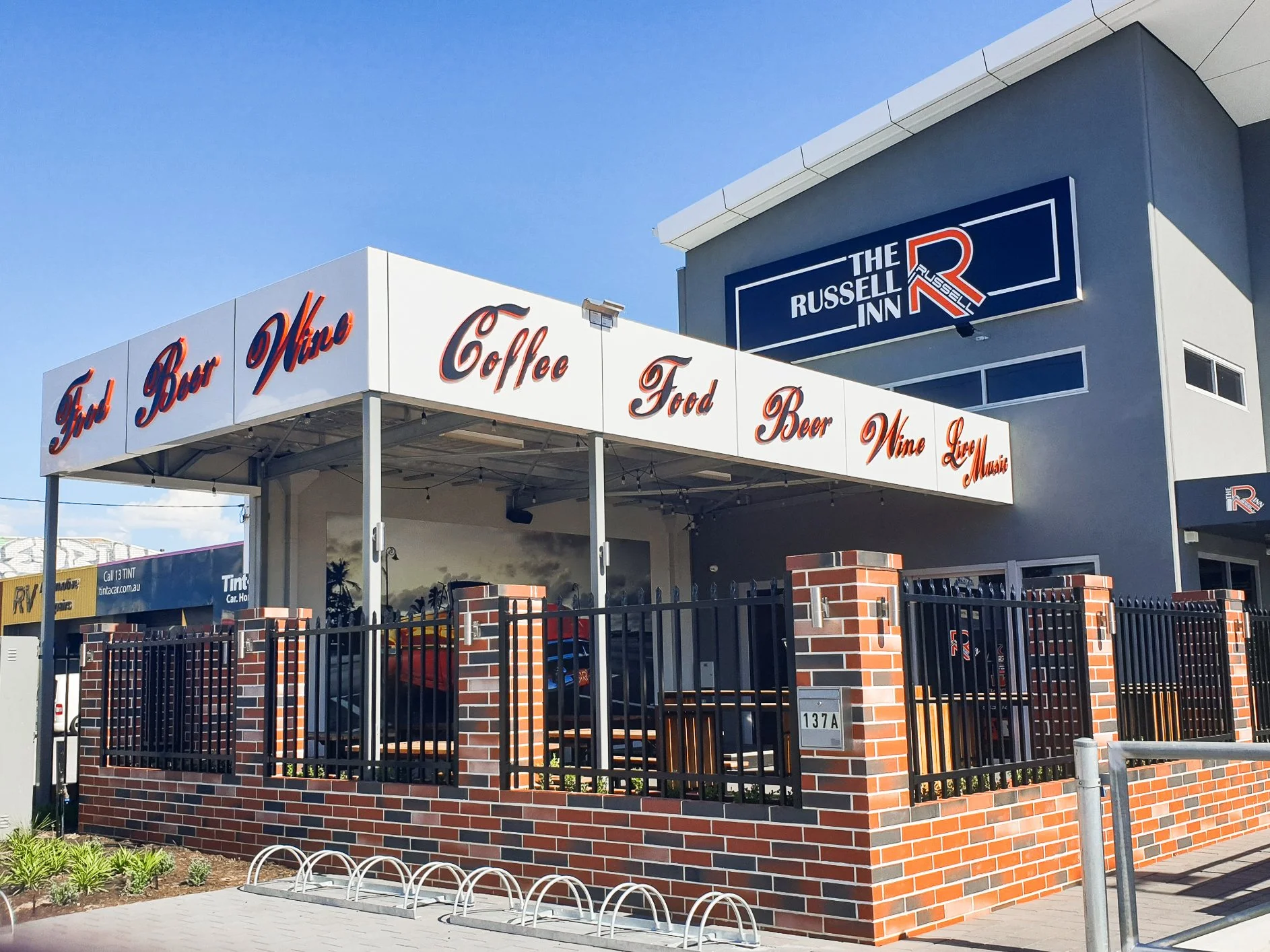 Exterior of a building with 3D signs advertising food, beer, wine, coffee, liquor, music, and a hotel called The Russell Inn. Business Signage and branding solutions