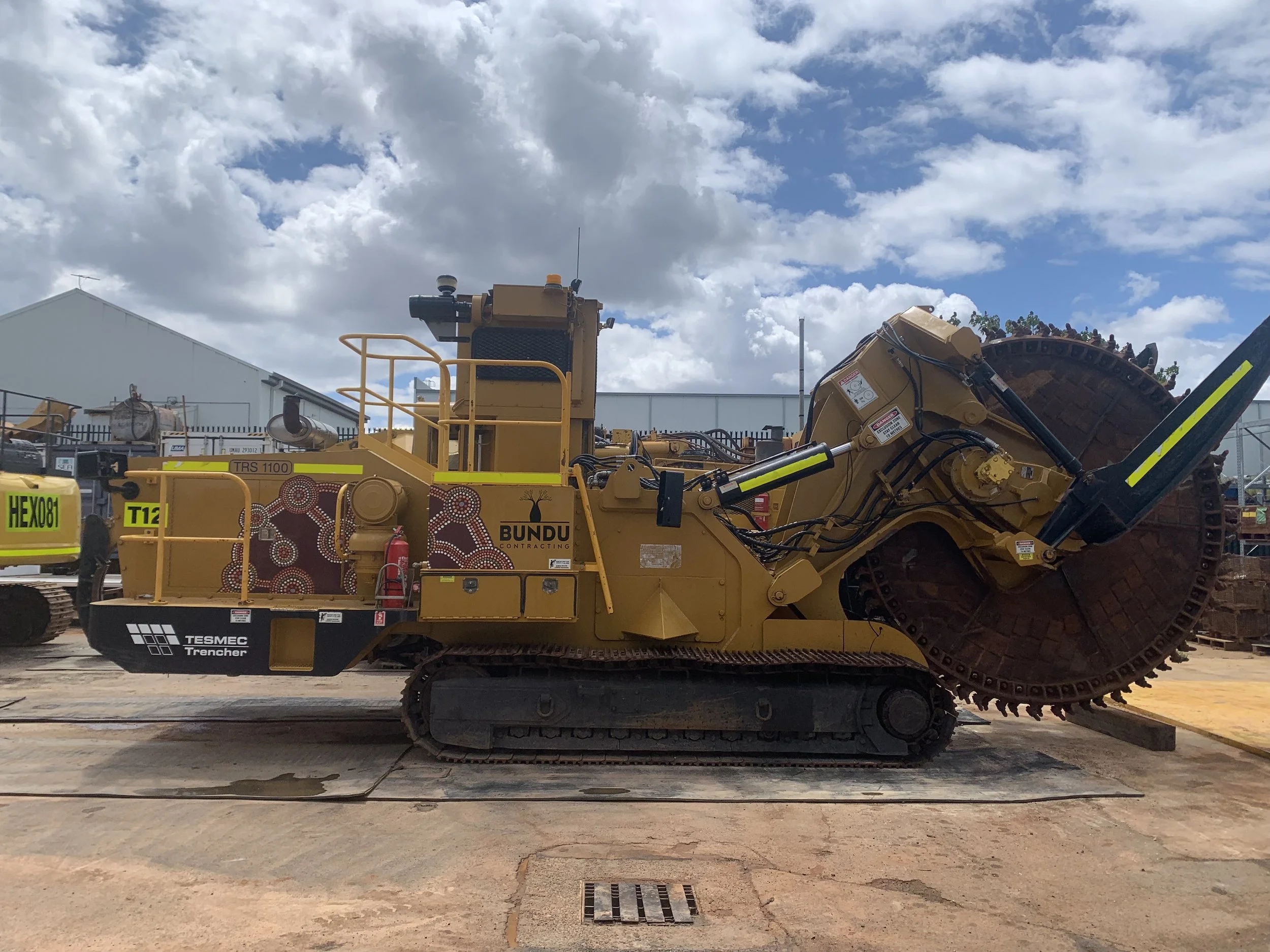 A large yellow mining earth cutting machine, with tracks and a large grinding drum fitted with high quality branding and high-visibility DG3 striping and Asset Numbers.