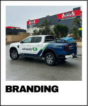 White pickup truck with blue and green branding parked outside a commercial building with large red and gray signage.