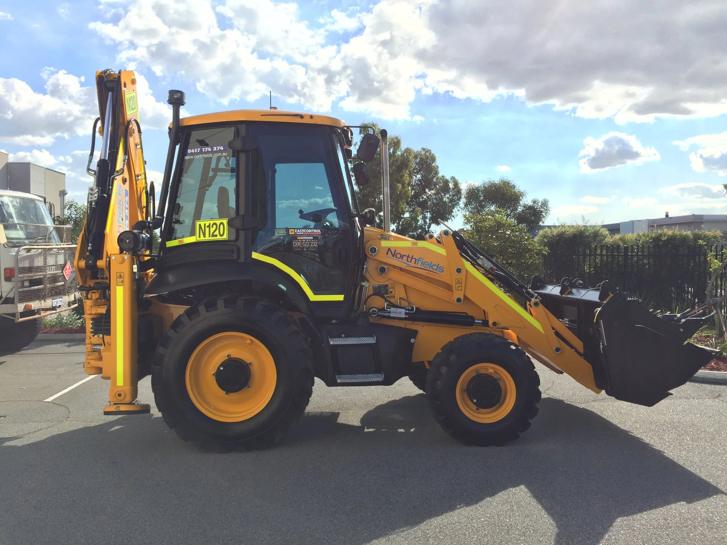 Yellow construction backhoe loader with the company branding 'Northfields' on it with high-visibility DG3 striping.