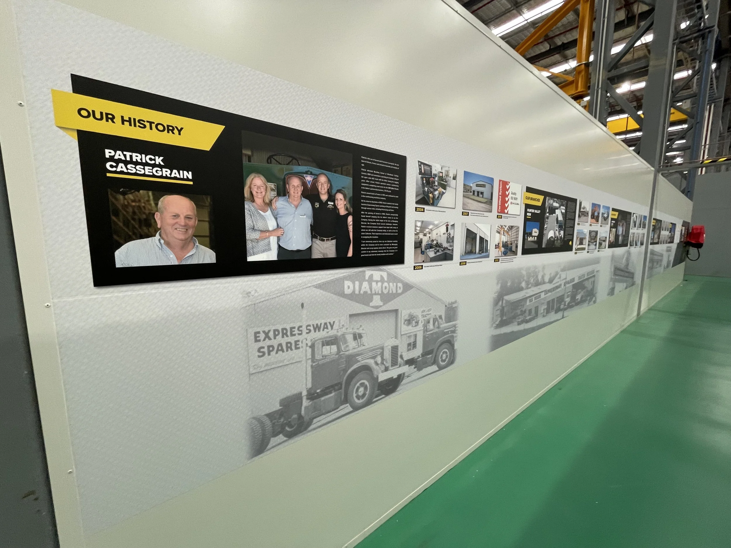 Long wall signage showing 'Our History' featuring photos and information about Patrick Cassegrain, including a portrait and a group photo. Decorative wall graphic signage