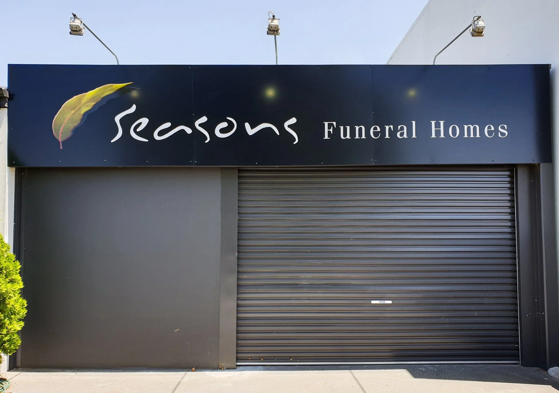 Storefront with a black sign that reads 'Seasons Funeral Homes' and features a decorative leaf logo. Fascia Business Signage