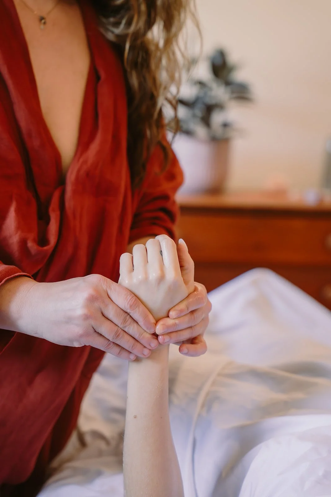 A person in an orange jacket is holding and comforting a person's hand, who is lying in bed.