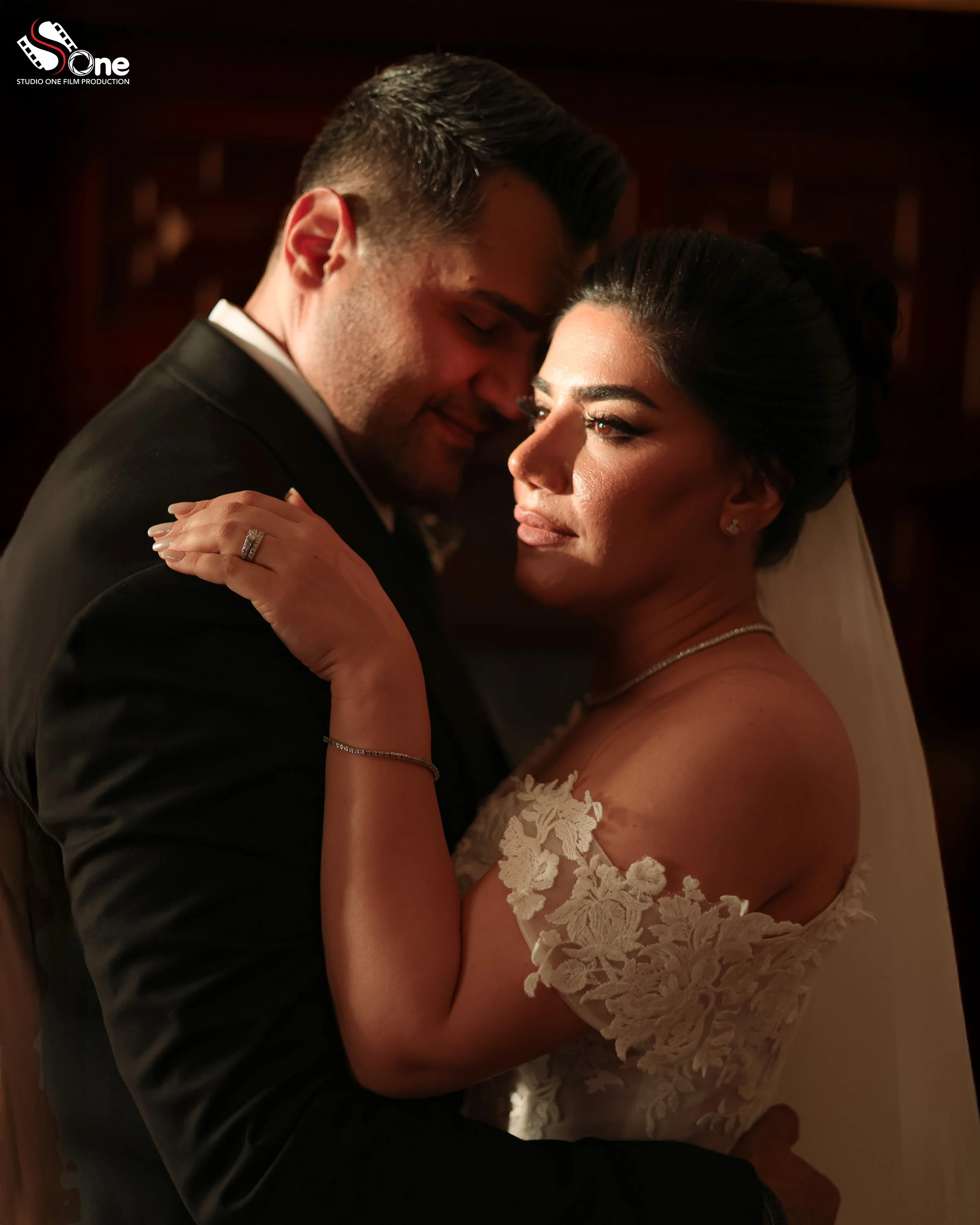 A bride and groom embrace closely, sharing an intimate moment during their wedding, with warm, soft lighting highlighting their faces and wedding attire.