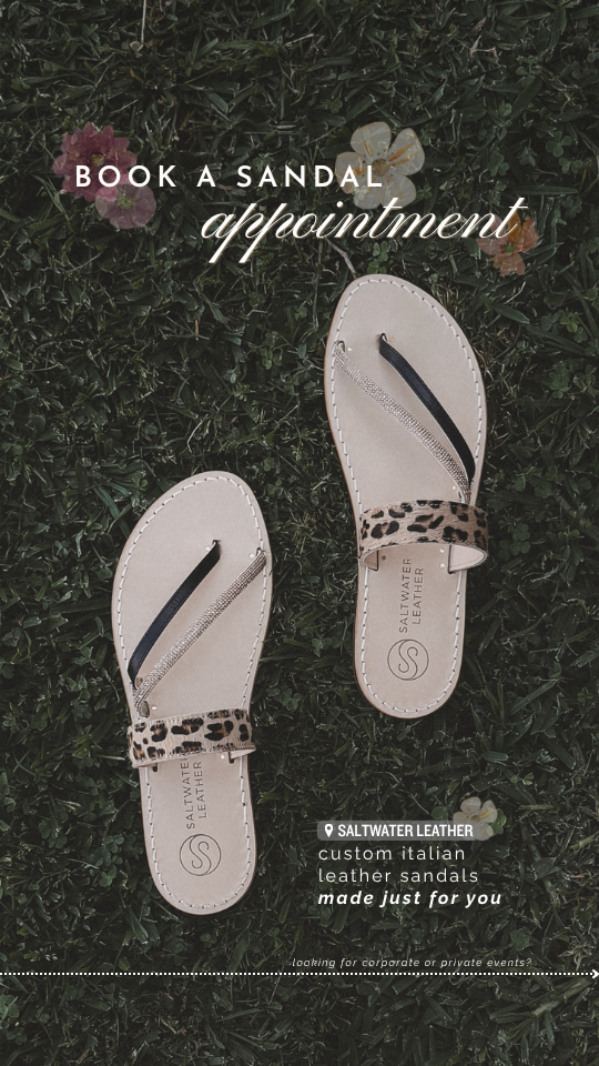 Pair of beige leather sandals with leopard print straps, placed on grass with small flowers. Text overlay promotes booking an appointment with Saltwater Leather for custom Italian leather sandals.