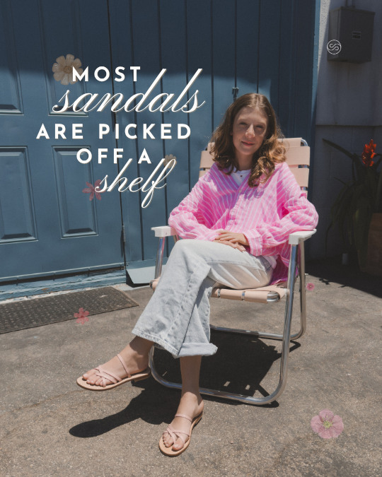 Woman sitting on a chair outside in front of a blue door, wearing a pink sweater and white pants, with text overlay that reads 'Most sandals are picked off a shelf', and pink flowers digitally added around her.