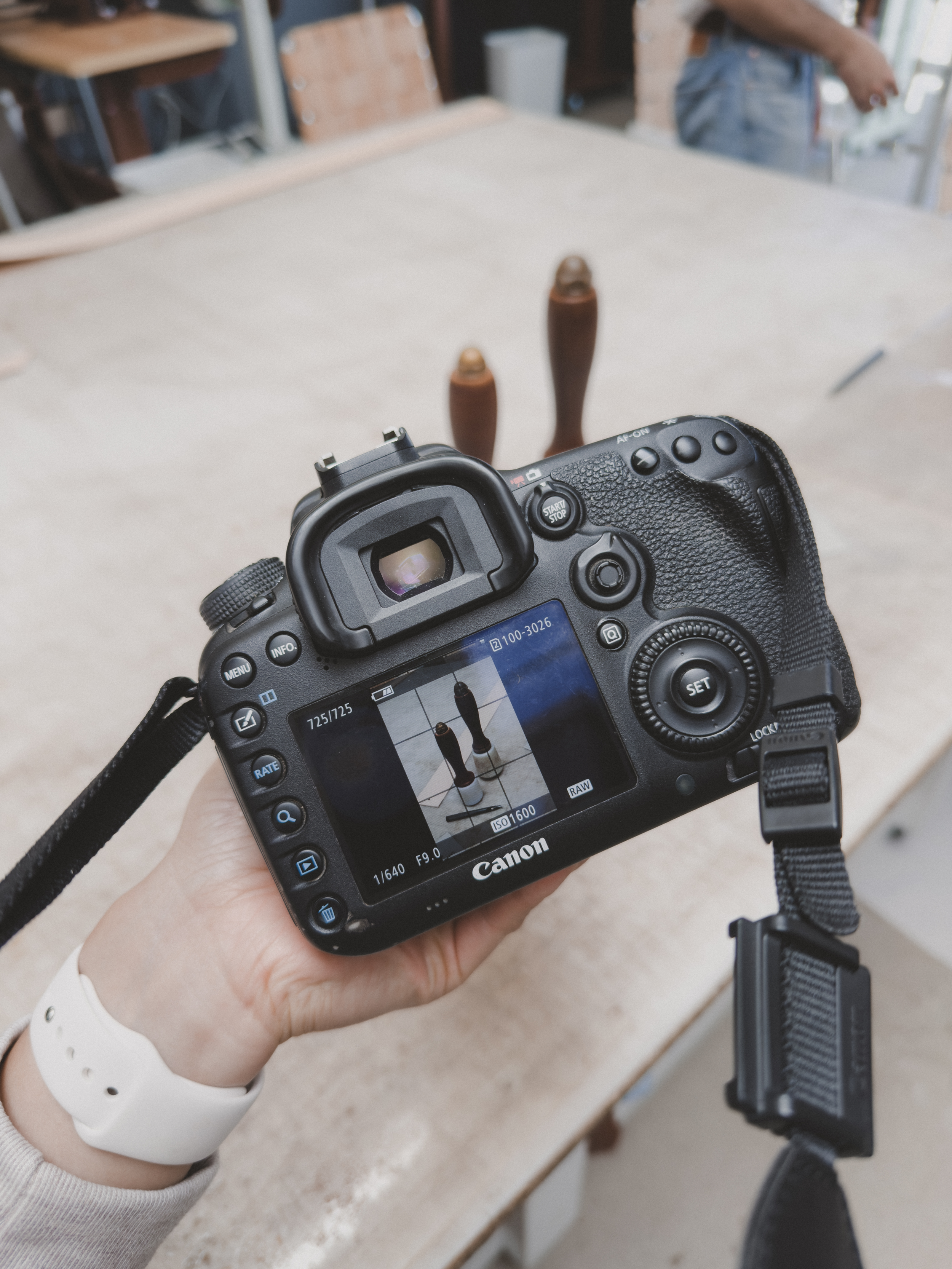 Close-up of a digital camera capturing an image inside a workshop, with two wooden tools spaced apart in the background and a person using the camera.