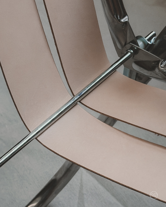 Close-up of a beige chair with a metal pole running through its seat and a chrome leg.