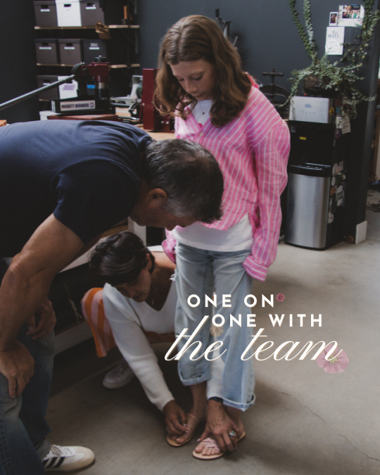A man, a young girl, and a woman are in a room, with the girl rolling up her pant leg while the man and woman assist. The room has office supplies and a water cooler in the background. Text overlay says, "One on one with the team."