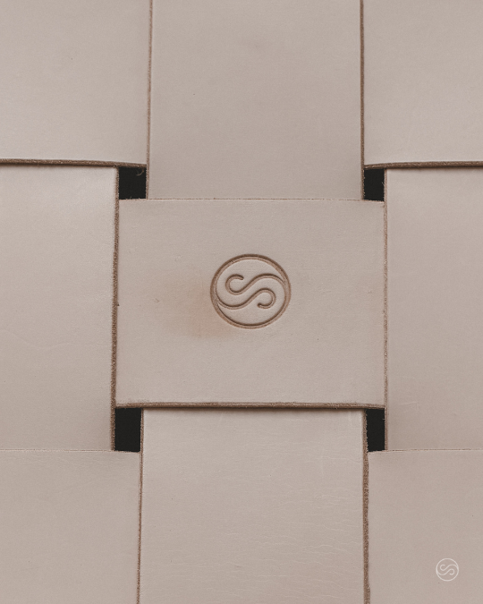 Small white tile with a circular logo featuring a stylized letter S in the center, surrounded by a carved border.