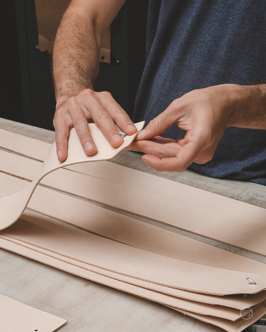 Person working on leather straps at a workbench, possibly in a leather workshop.